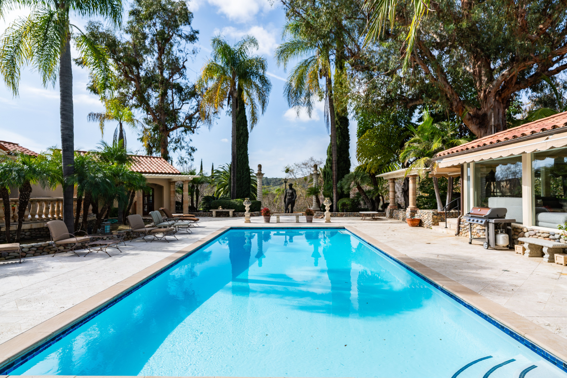 Nearby, the pool terrace centers on a saline swimming pool and spa, where columns and sculptures frame the deck, and a statue of Neptune stands at the far end overlooking the water.