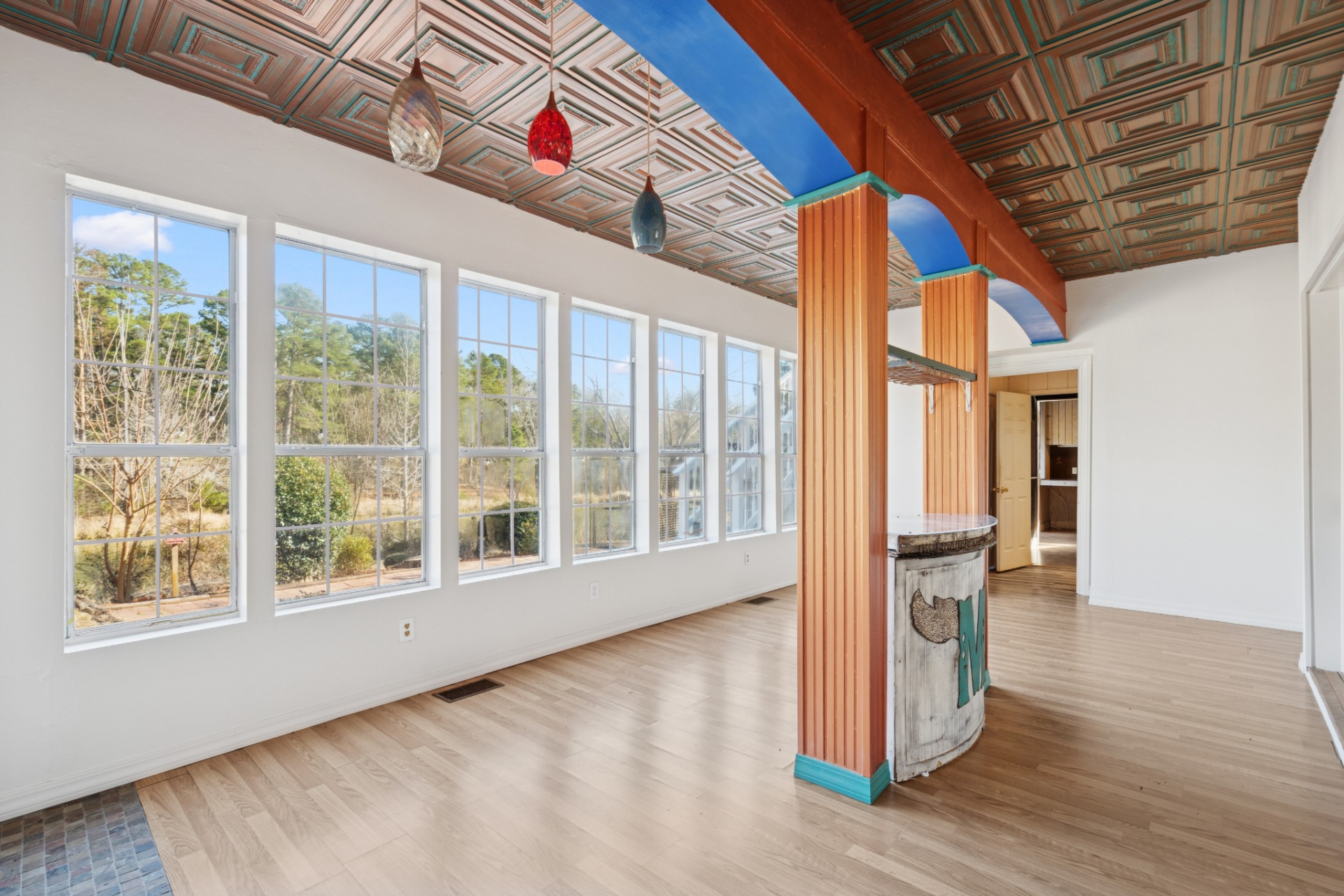 The space is defined by a built-in bar with a curved front, positioned beneath a coffered ceiling with painted detailing that adds a pop of color overhead.