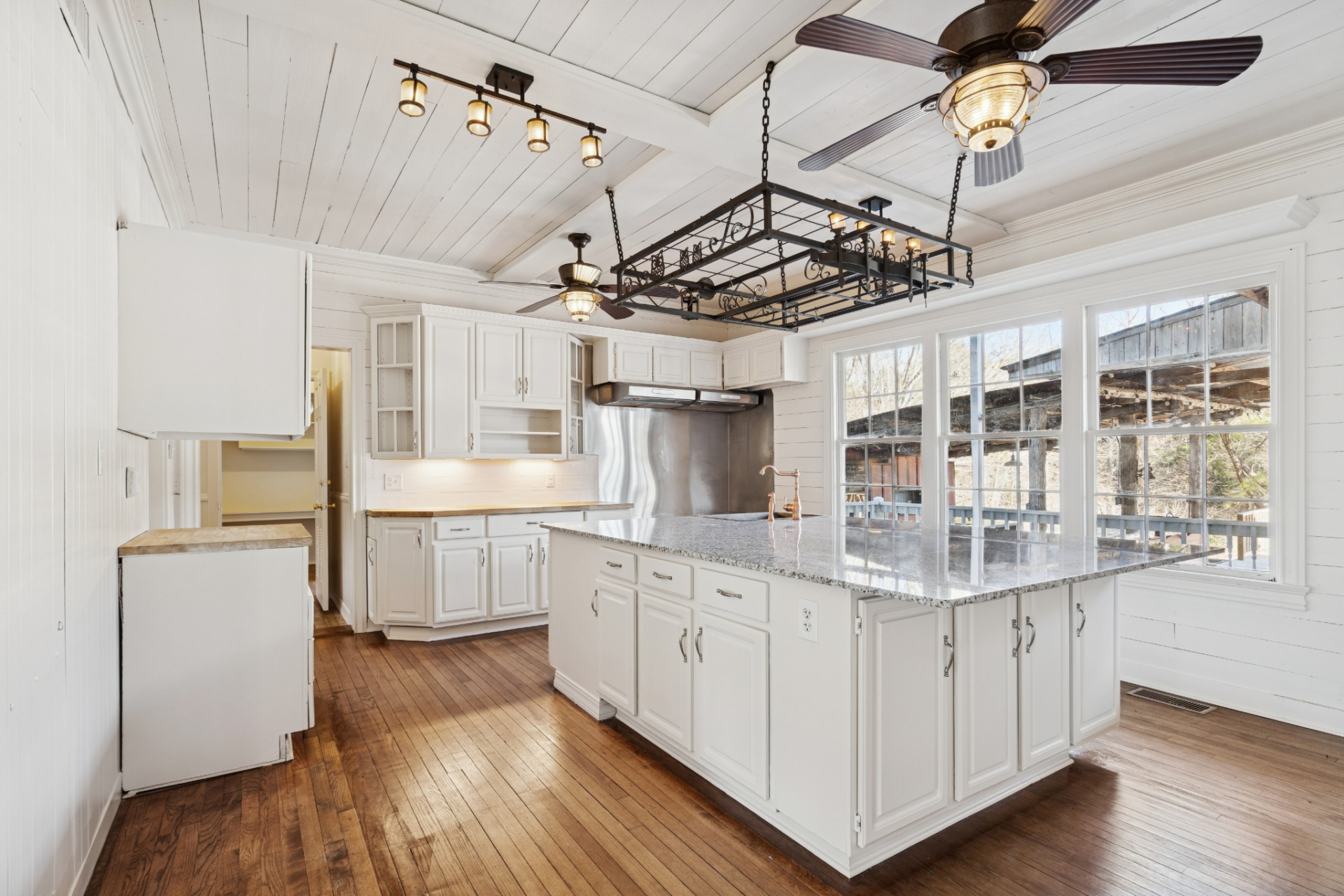 A large central island anchors the space, topped with stone countertops and fitted with a farmhouse-style sink, offering both prep space and room to gather.