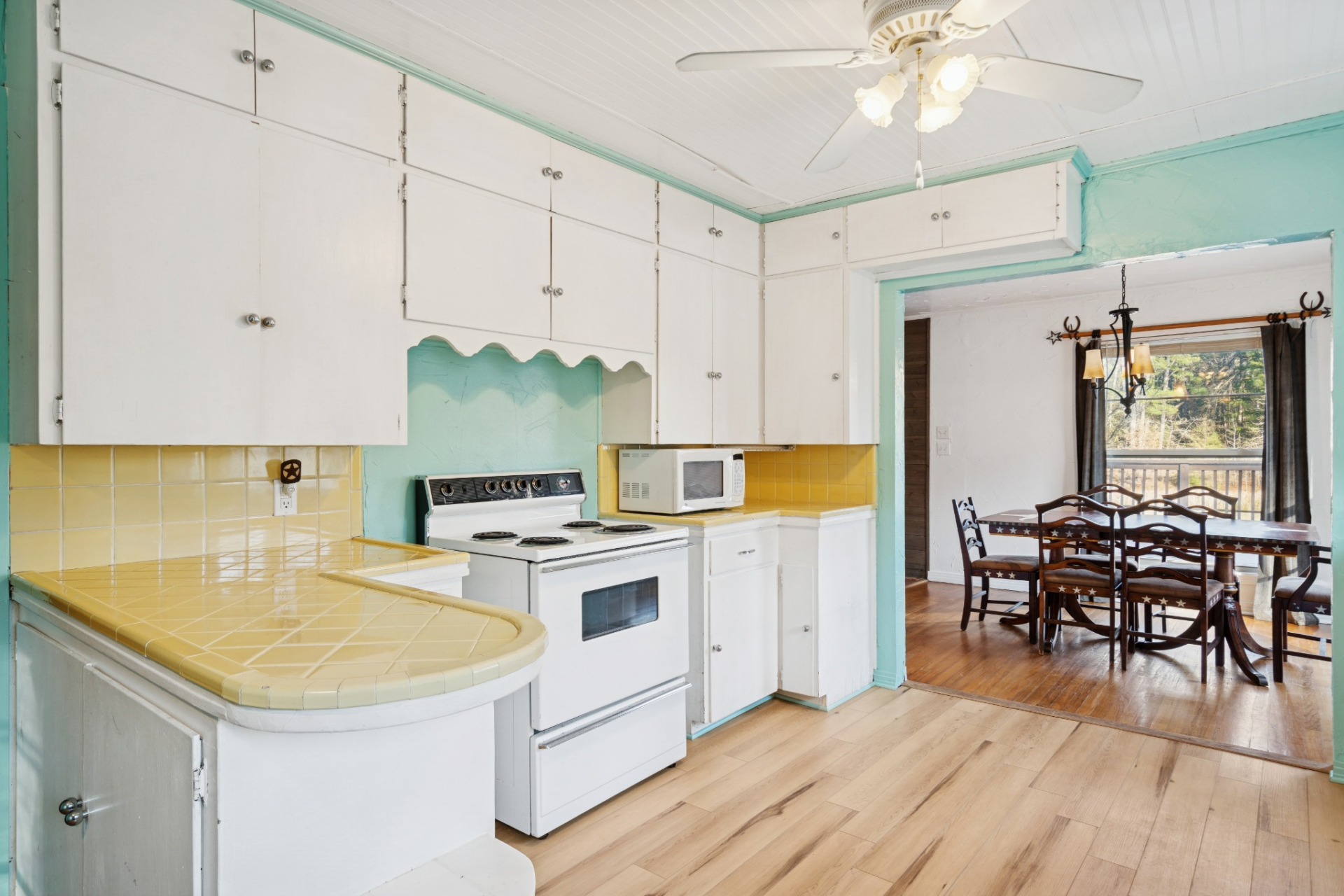 In the next room, the kitchen features a mix of white cabinetry, yellow tile countertops, and turquoise accent walls that give the space a more vivid and colorful personality than the other rooms.