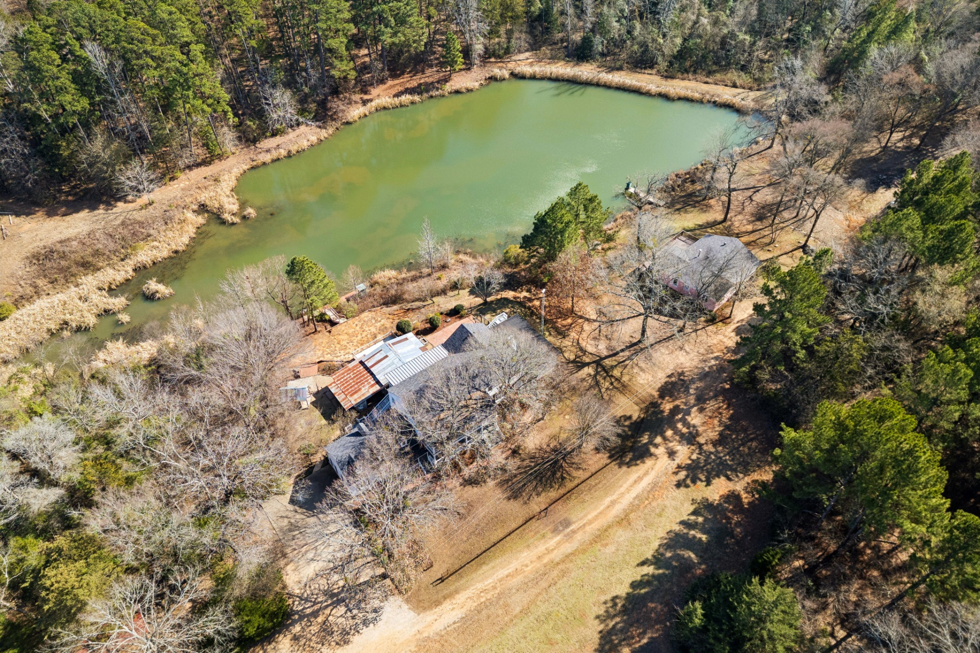 A three-acre stocked pond sits at the center of the property, bordered by trees and natural brush, with open sightlines that extend across the water and surrounding acreage.