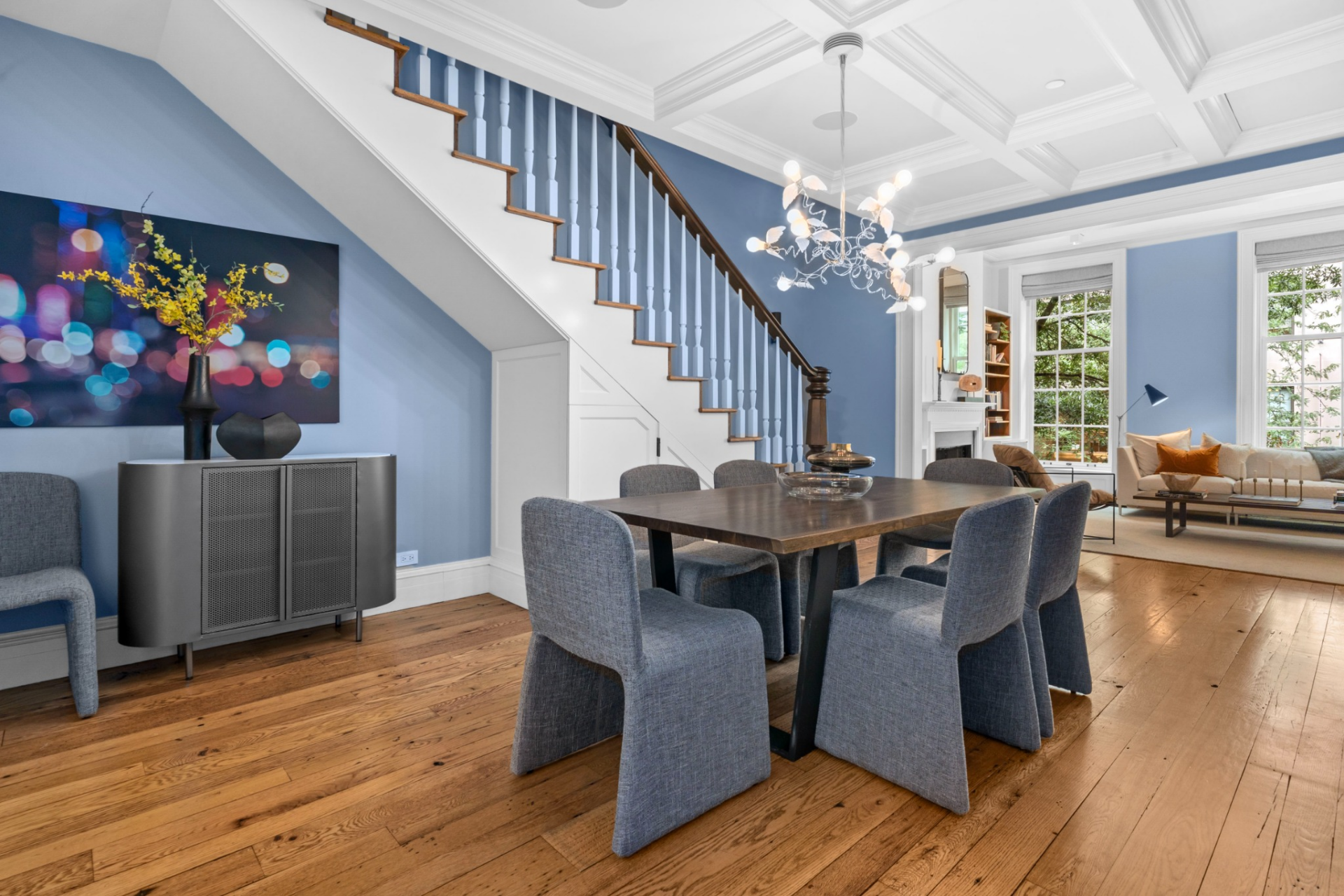 A rectangular table sits beneath a modern chandelier, while the coffered ceiling above adds depth and structure to the space.