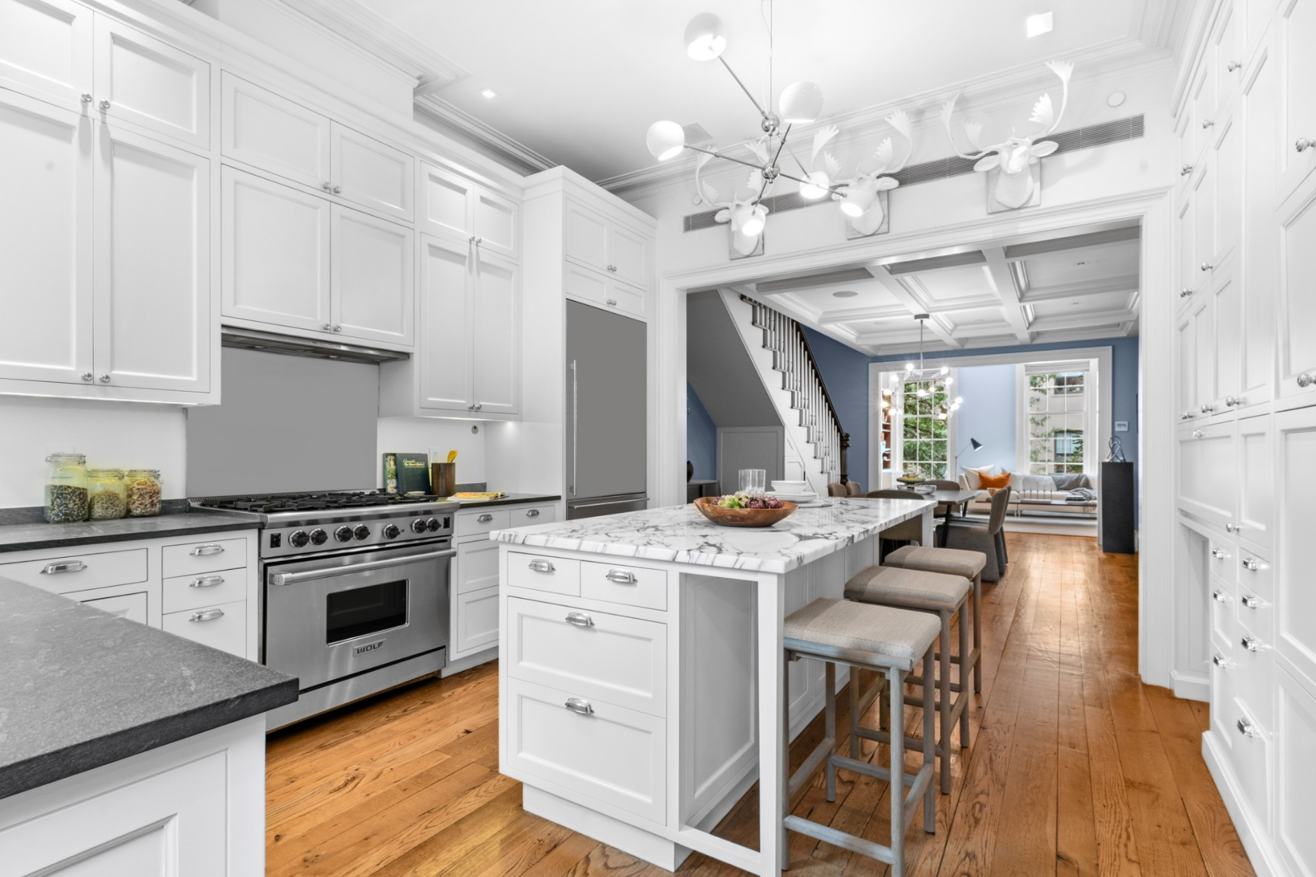 A marble-topped island sits at the center, fitted with seating for casual dining, while high-end appliances from Wolf, Sub-Zero, and Miele are integrated throughout the space.