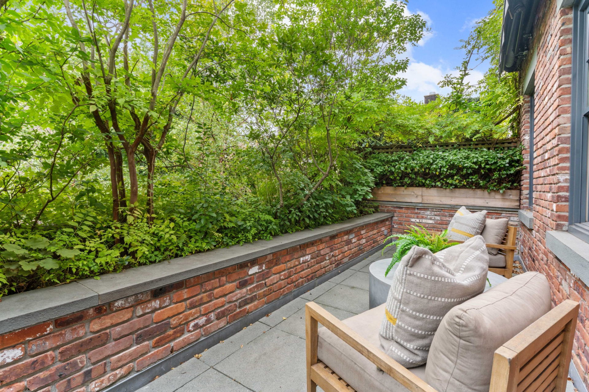 Just off the bedroom, the private terrace is framed by brick walls and dense greenery, creating a tucked-away outdoor space.