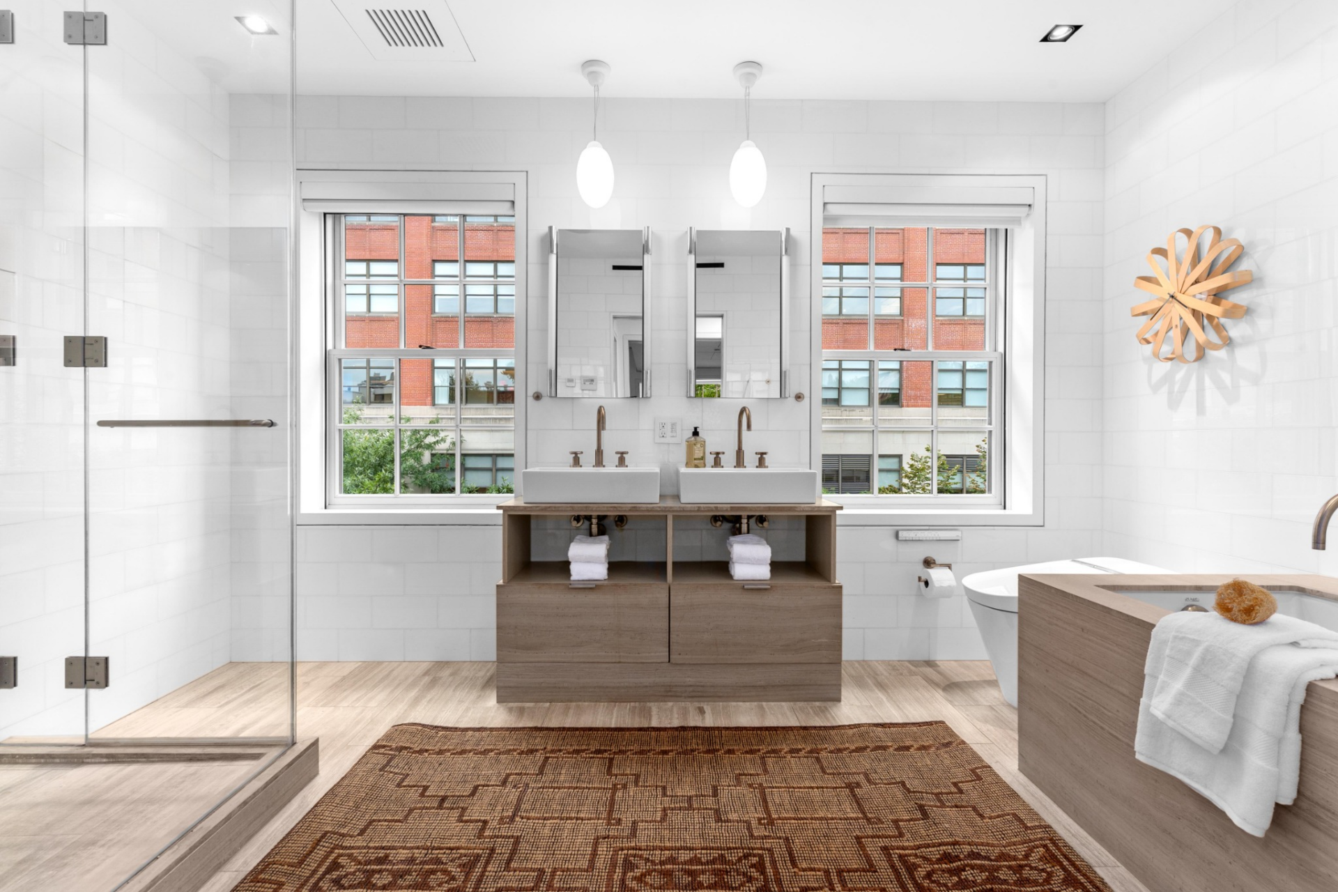 Completing the suite, the bathroom is finished in marble and light wood tones, centered around a double vanity with clean-lined fixtures and mirrored cabinetry.