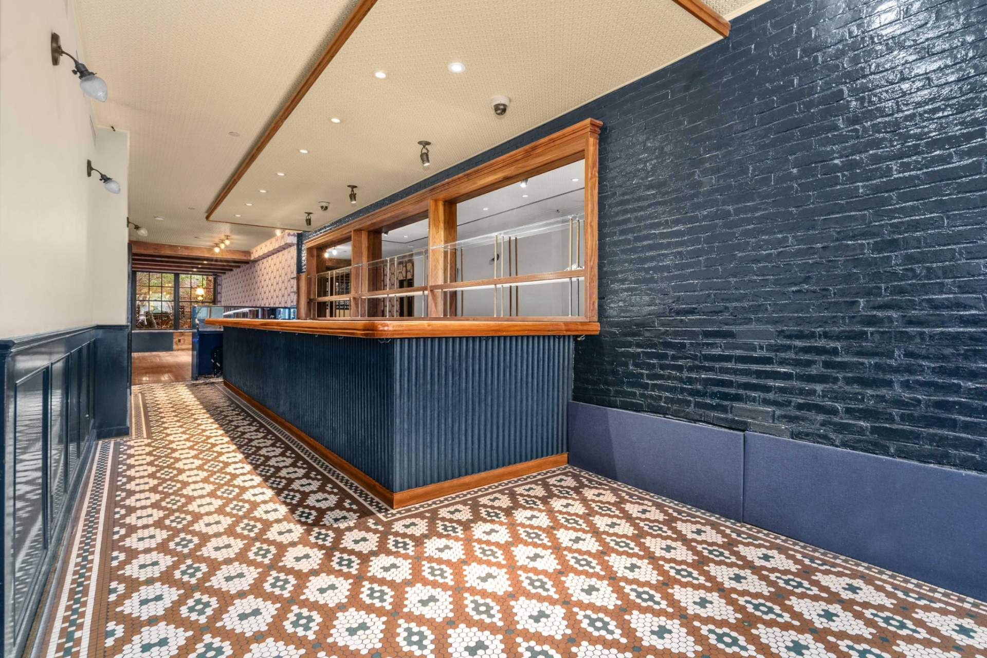 Inside, the space blends character and function, from patterned tile flooring and dark painted brick to wood-framed service windows and a long bar.