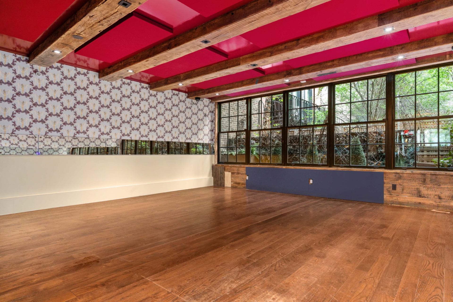 Toward the rear, a more open dining area sits beneath exposed beams and bold ceiling accents, with large windows bringing in natural light and connecting back to the garden beyond.