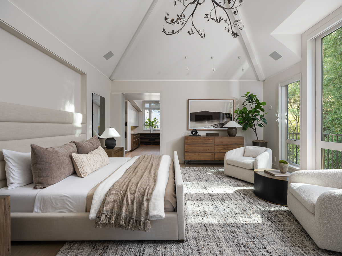 Upstairs, the primary suite is set beneath a vaulted, cathedral-style ceiling that opens the room vertically, with exposed structure and a central light fixture drawing the eye upward. 
