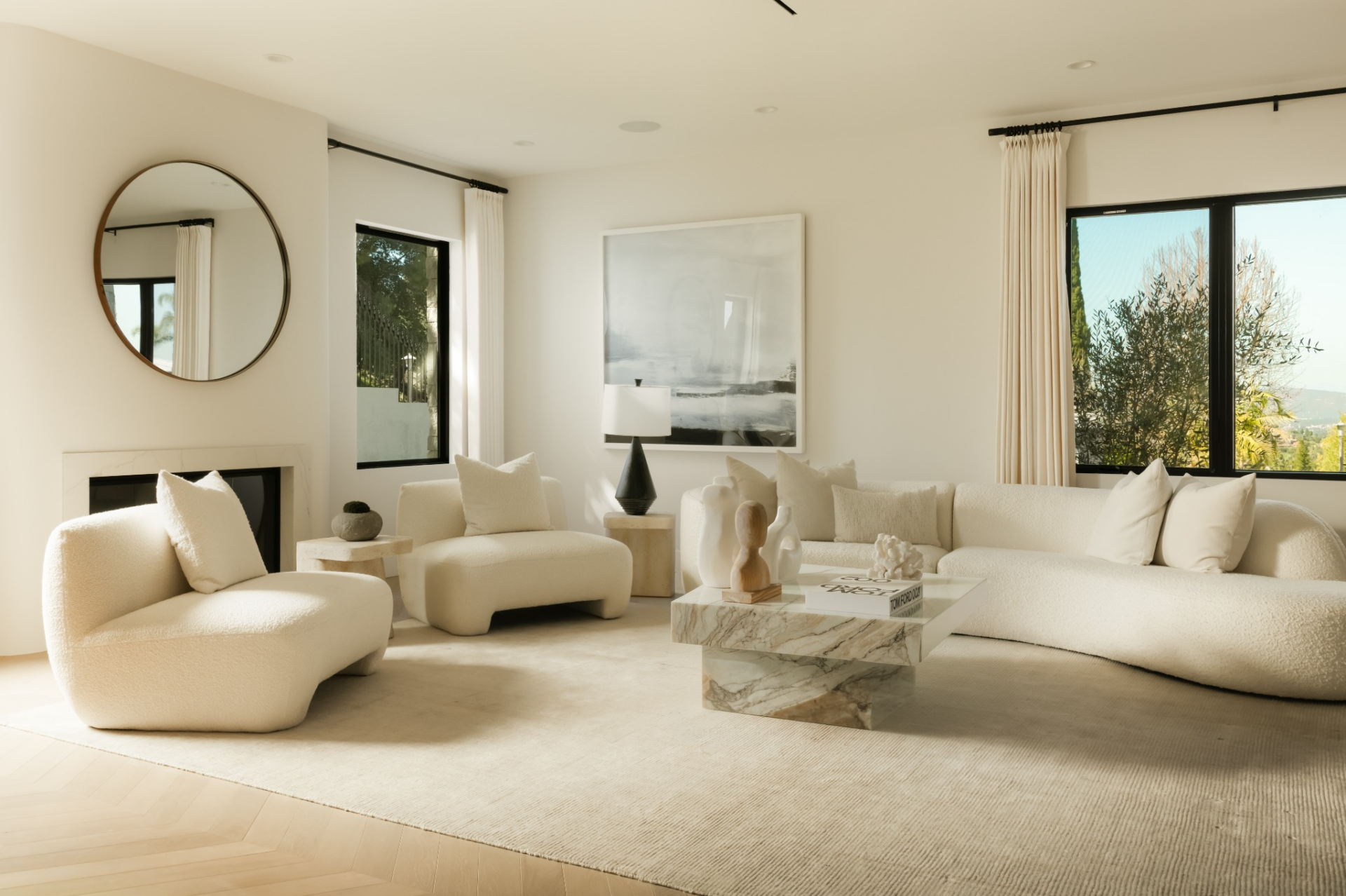 Herringbone wood flooring runs throughout, grounding a seating arrangement of low-profile sofas and chairs centered around a stone coffee table.