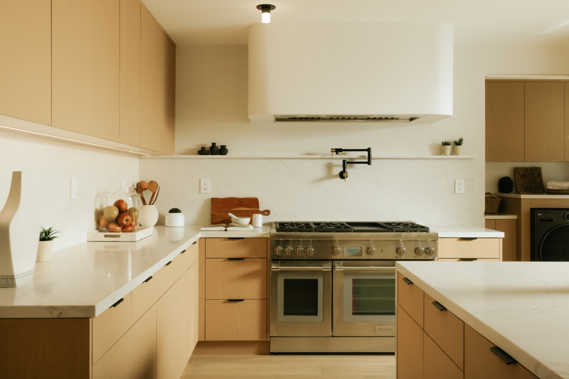 Integrated high-end appliances, including a professional-grade range and built-in refrigeration, are paired with a full-height stone backsplash and a sculptural vent hood that anchors the cooking area.