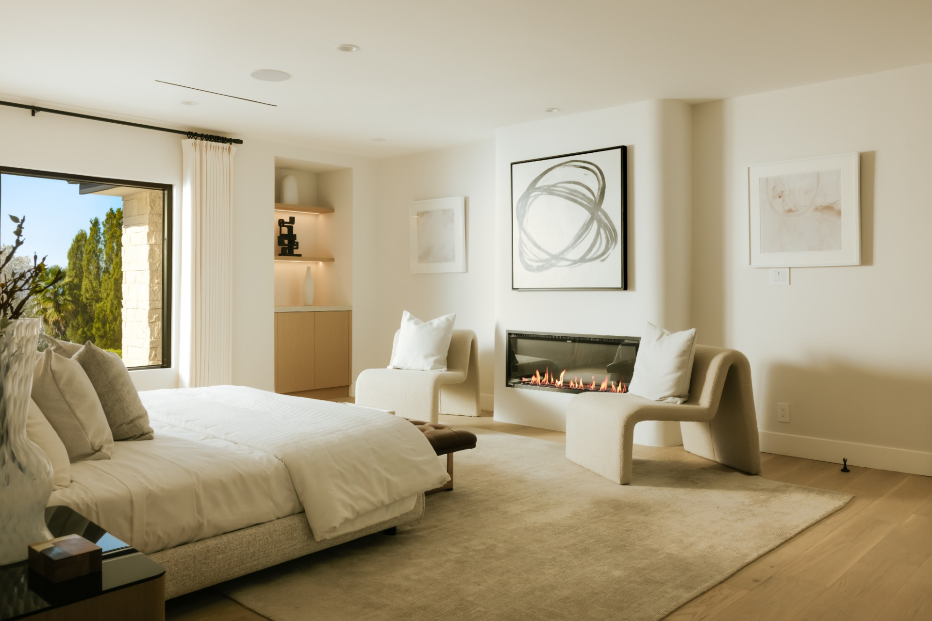 A linear fireplace is built into one wall, paired with two sculptural lounge chairs that create a secondary seating area, while integrated shelving and minimal artwork.