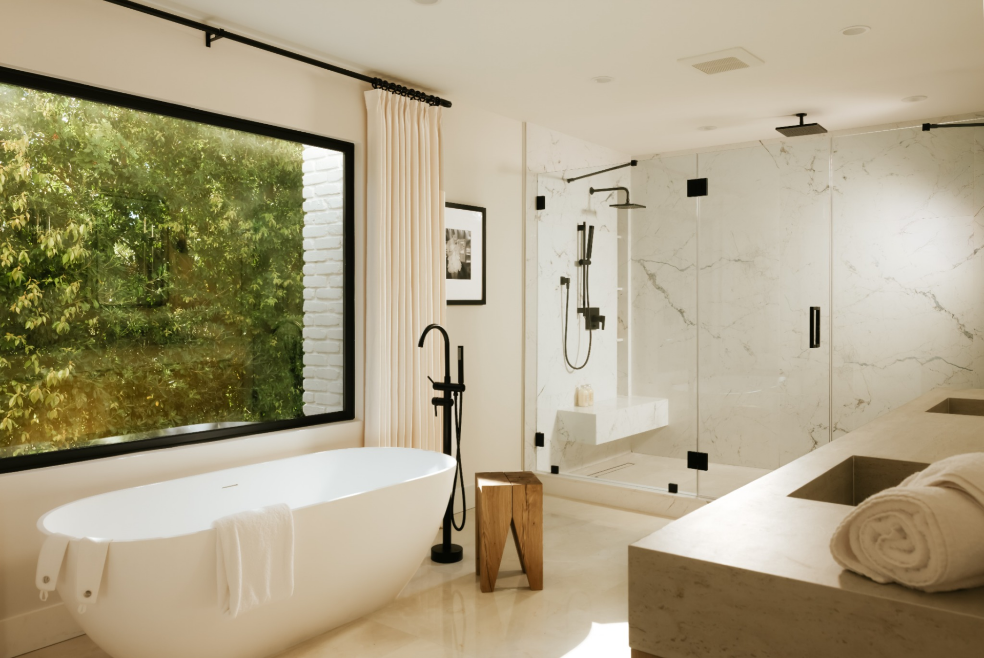  A freestanding soaking tub is positioned directly beneath a large picture window, set beside a floor-mounted black fixture. 