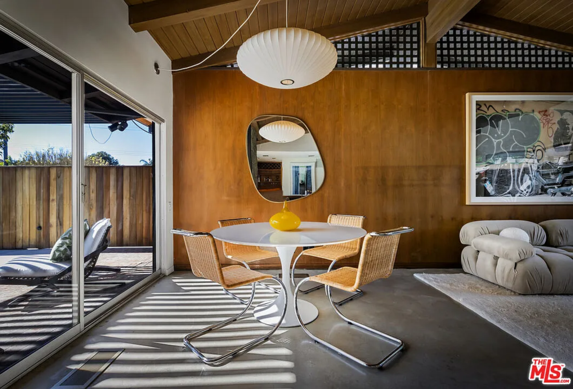 Next to it, the casual dining area includes a round table with woven chairs beneath a suspended globe pendant. 