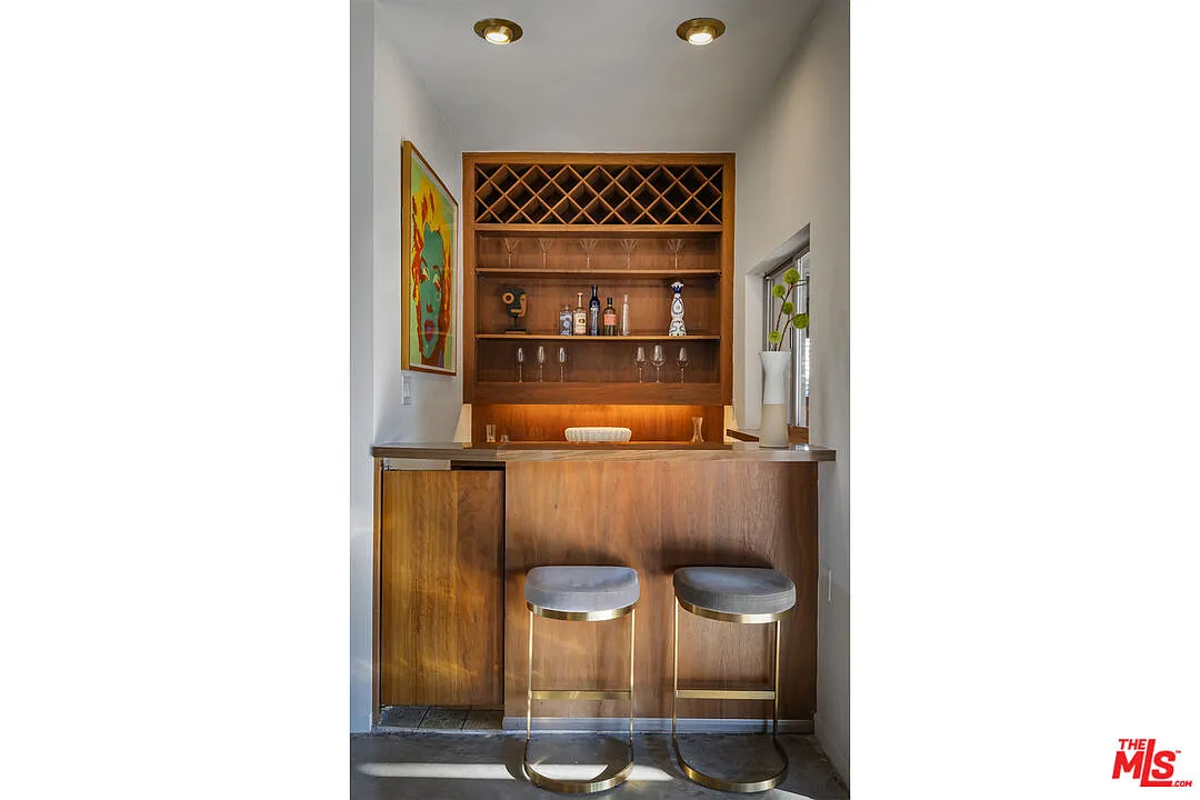 At the far end of the room, a built-in bar is set into a recessed niche, complete with wood cabinetry, open shelving, and a wine rack overhead. 