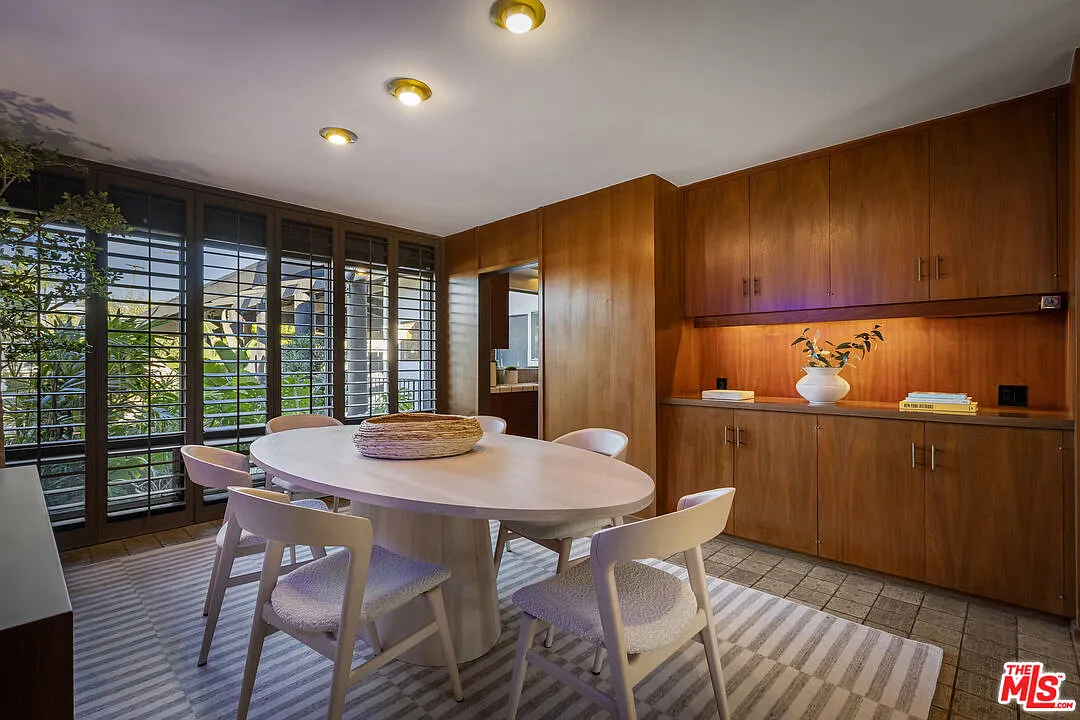 At the center, an oval dining table is positioned over a soft rug, surrounded by upholstered chairs that soften the room’s clean lines.
