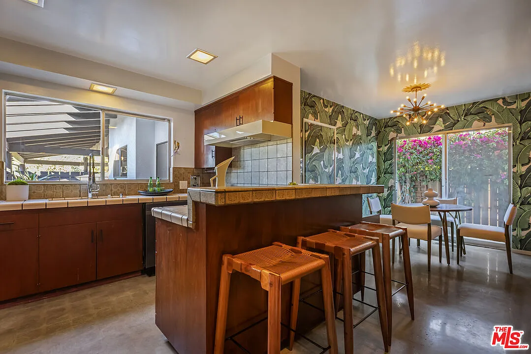 A peninsula with bar seating separates the kitchen from a casual breakfast nook set against bold, leafy wallpaper.