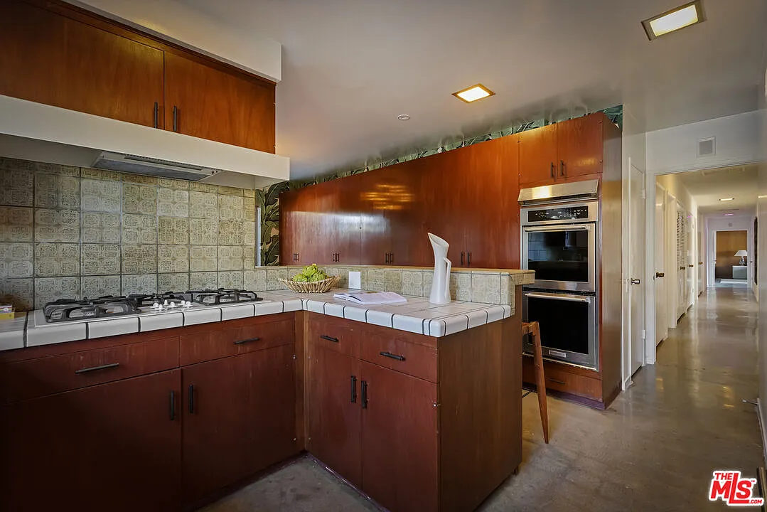 Through the dining room's small doorway, the teak kitchen is lined in rich wood cabinetry, paired with tiled countertops and backsplash that wrap the cooking area.