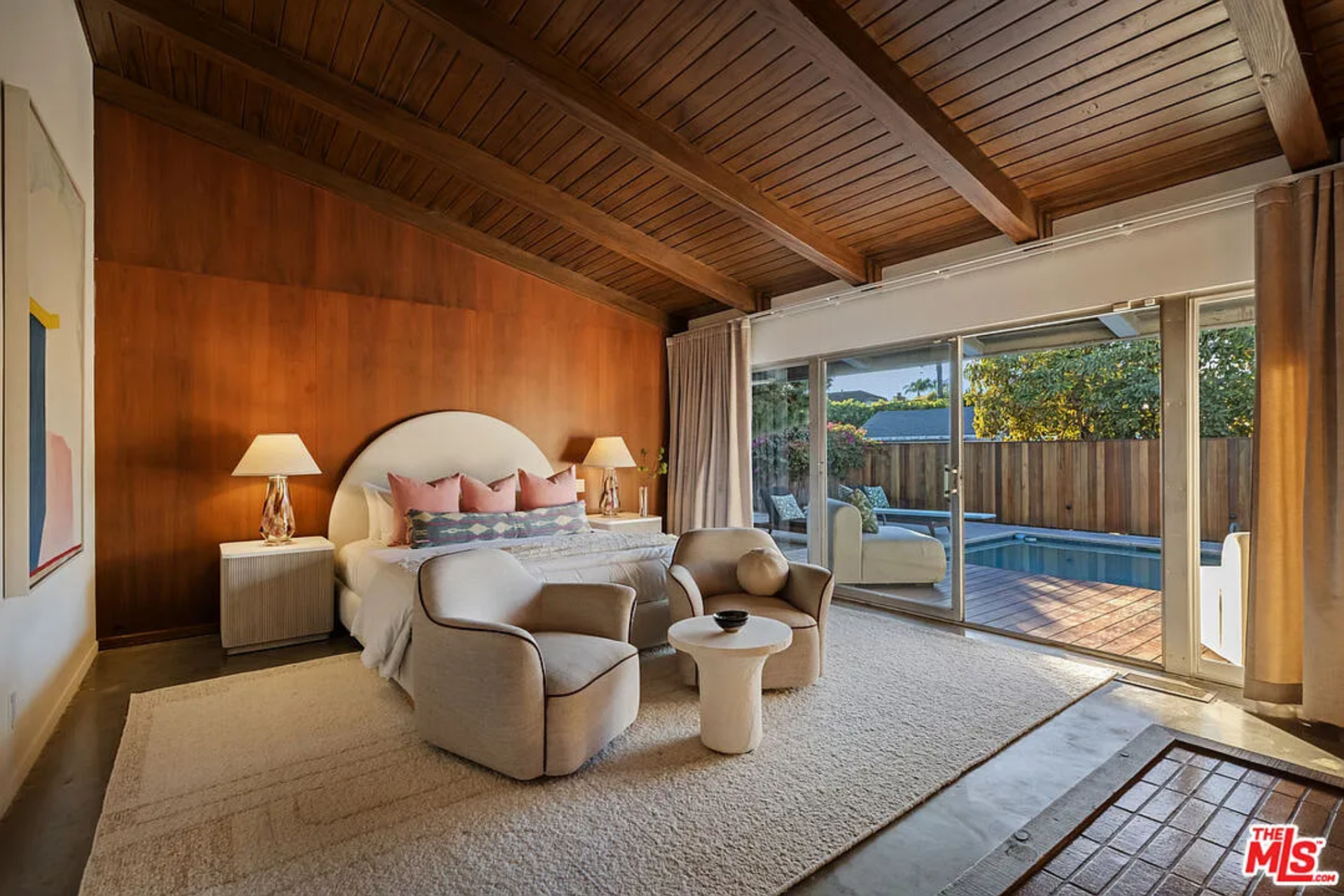 The bedroom itself is set against a full wall of warm wood paneling and exposed beam ceilings, with sliding glass doors opening directly to the pool deck.