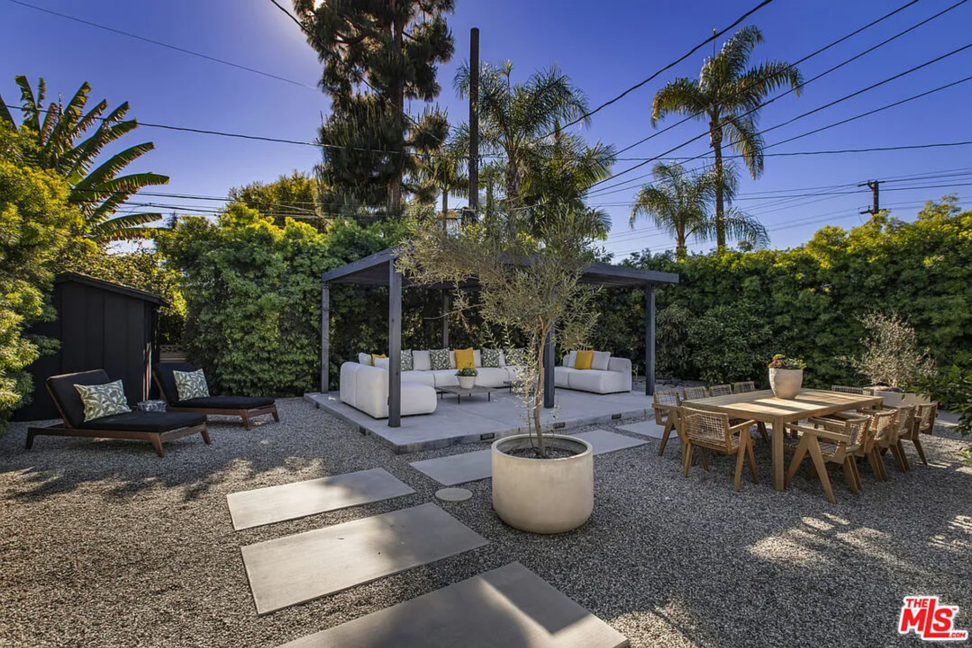 Tucked deeper into the yard, a separate lounge and dining space is set on a gravel courtyard beneath a simple pergola. 