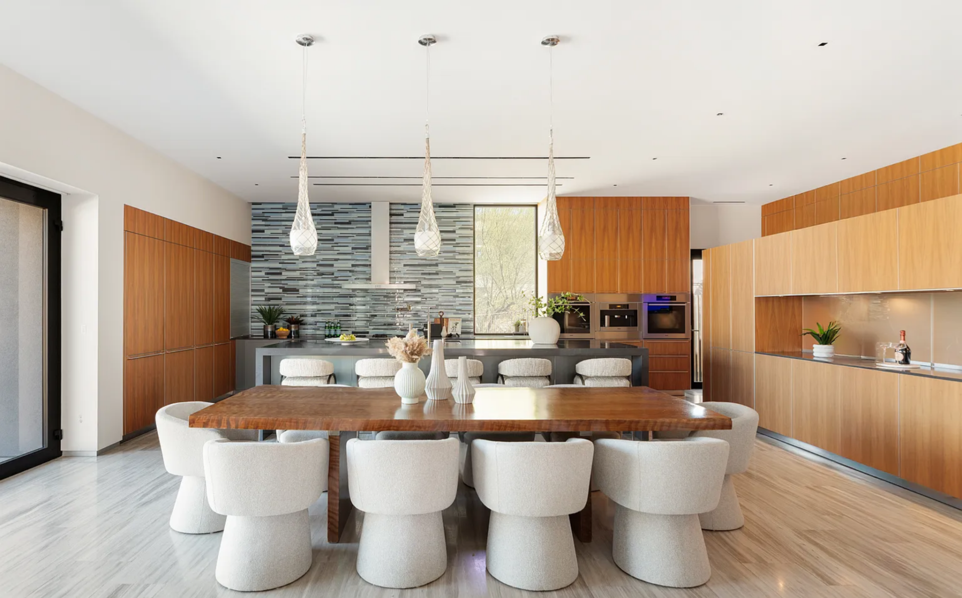 The dining area is positioned at the center of the open layout, with a large rectangular wood table surrounded by sculptural upholstered chairs with rounded bases.