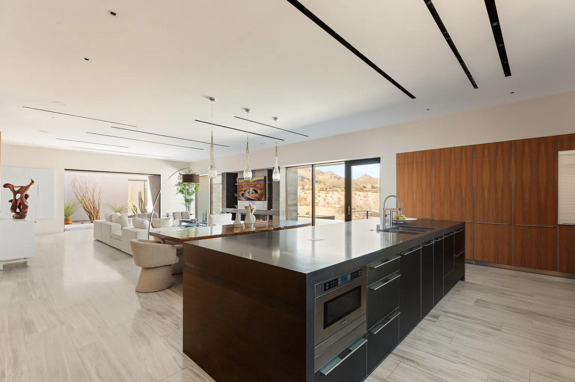 A large central island with a smooth, dark countertop provides lots of prep space and integrated seating, while sleek cabinetry in warm wood tones lines the walls, keeping storage clean.