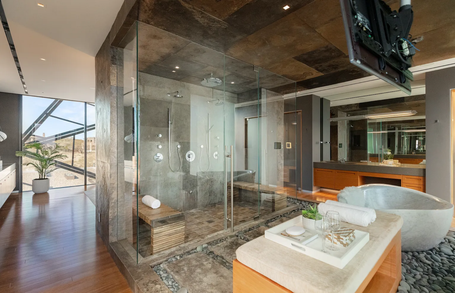 Behind the stone wall, the suite's bathroom features a glass-enclosed shower with dual shower heads and integrated bench seating. 