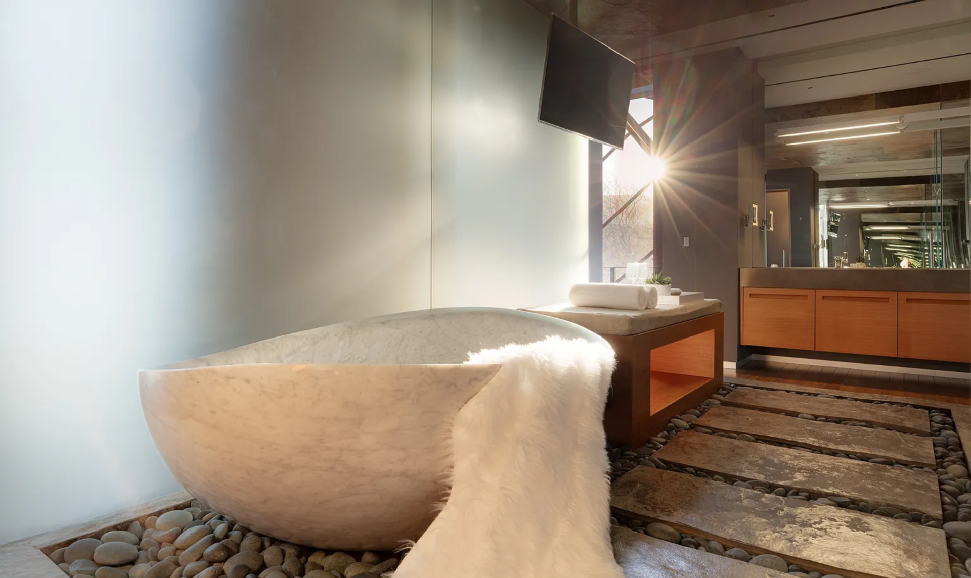 Just outside, the flooring shifts to large stone pavers set within river rock, guiding the layout toward a freestanding soaking tub positioned beside a frosted glass wall that filters in natural light.