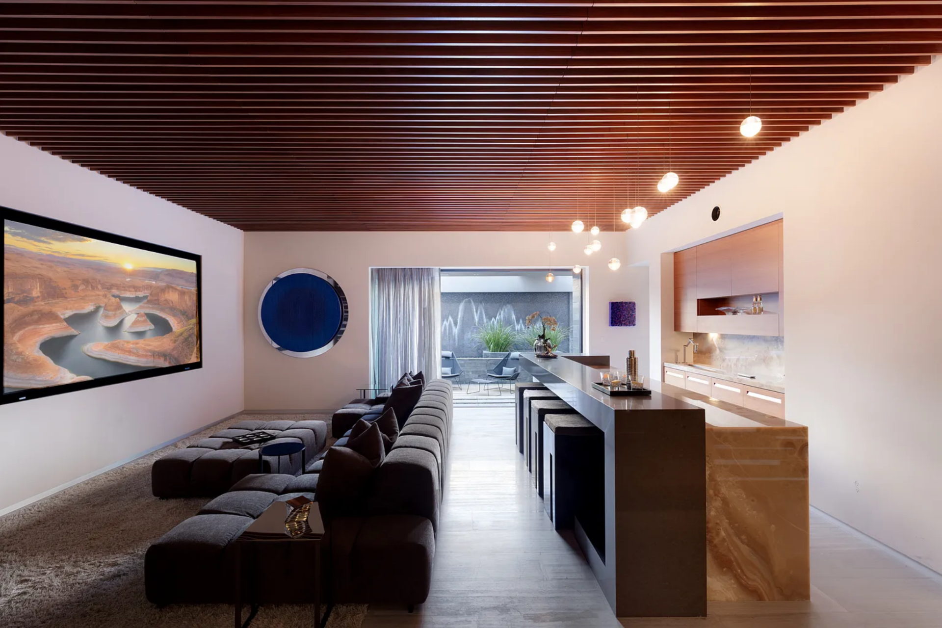 The layout flows directly into a built-in bar, where a stone counter extends the length of the space, lined with stools and softly lit by a series of pendant lights above.