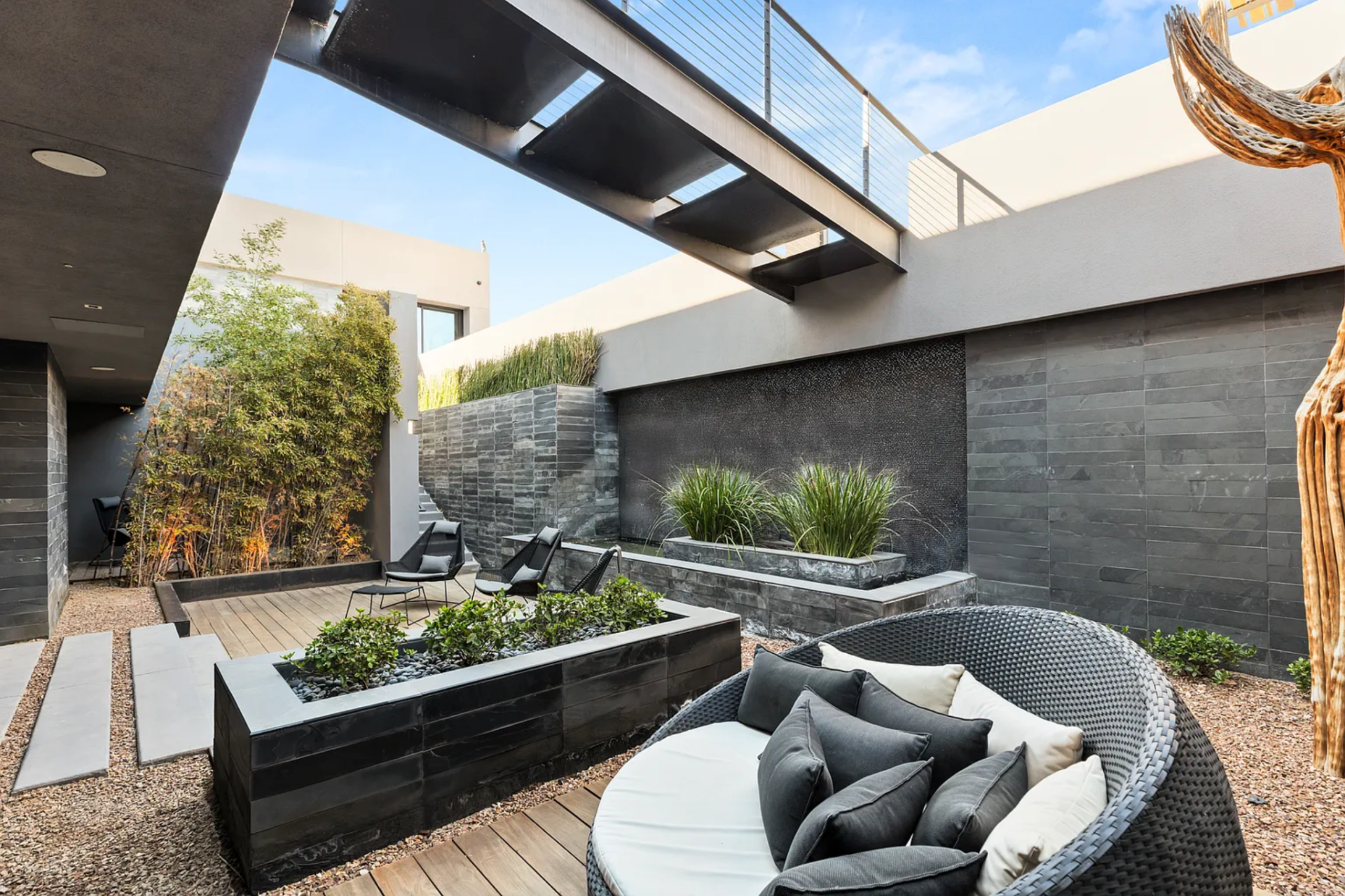 On the other side, the level opens to a private courtyard where a water feature runs along one wall, framed by layered stone and planters, with seating arranged across wood decking and gravel paths.