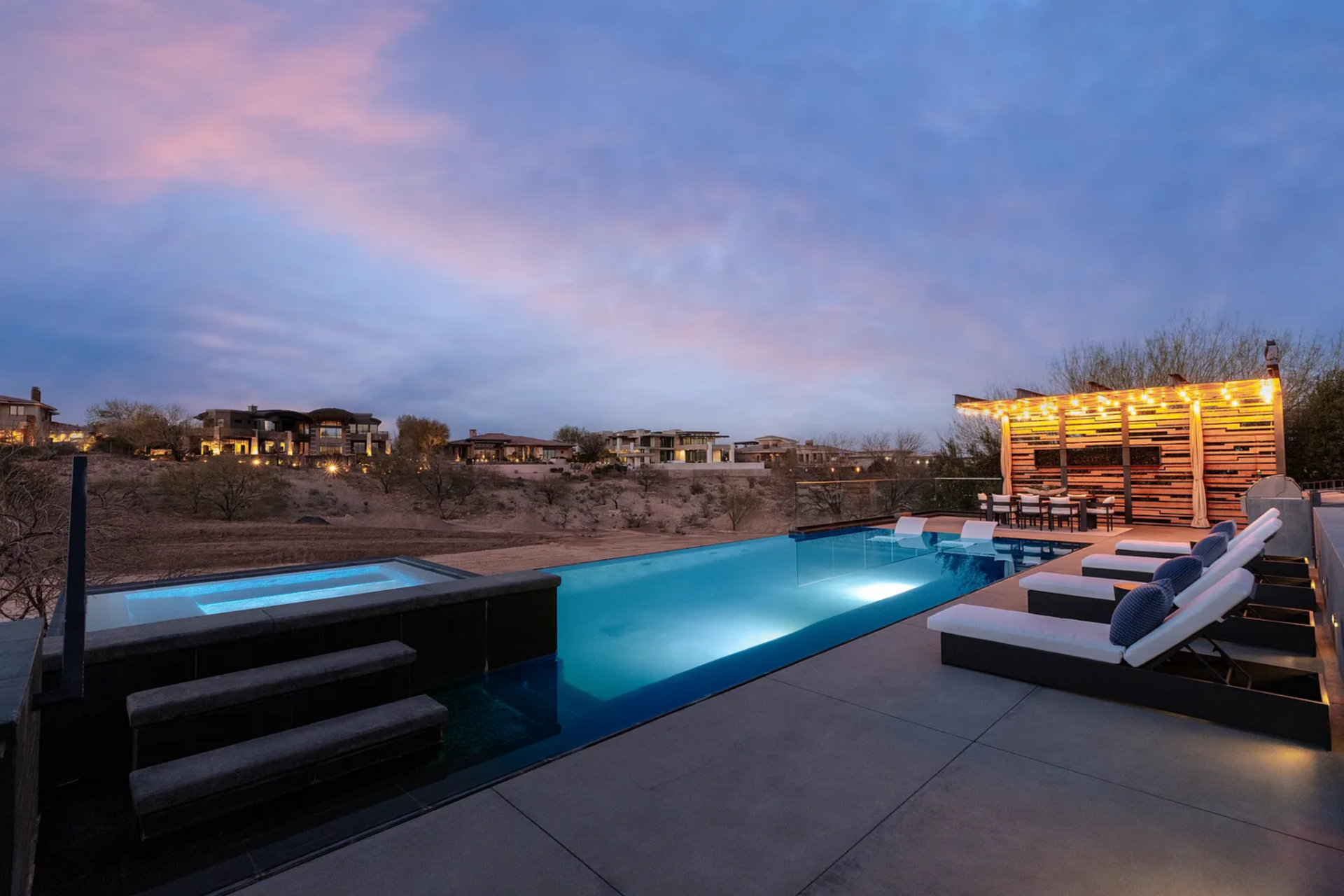 The backyard is built around a long, linear infinity-edge pool that stretches toward the desert, creating a clean visual line between the water and the surrounding landscape. 
