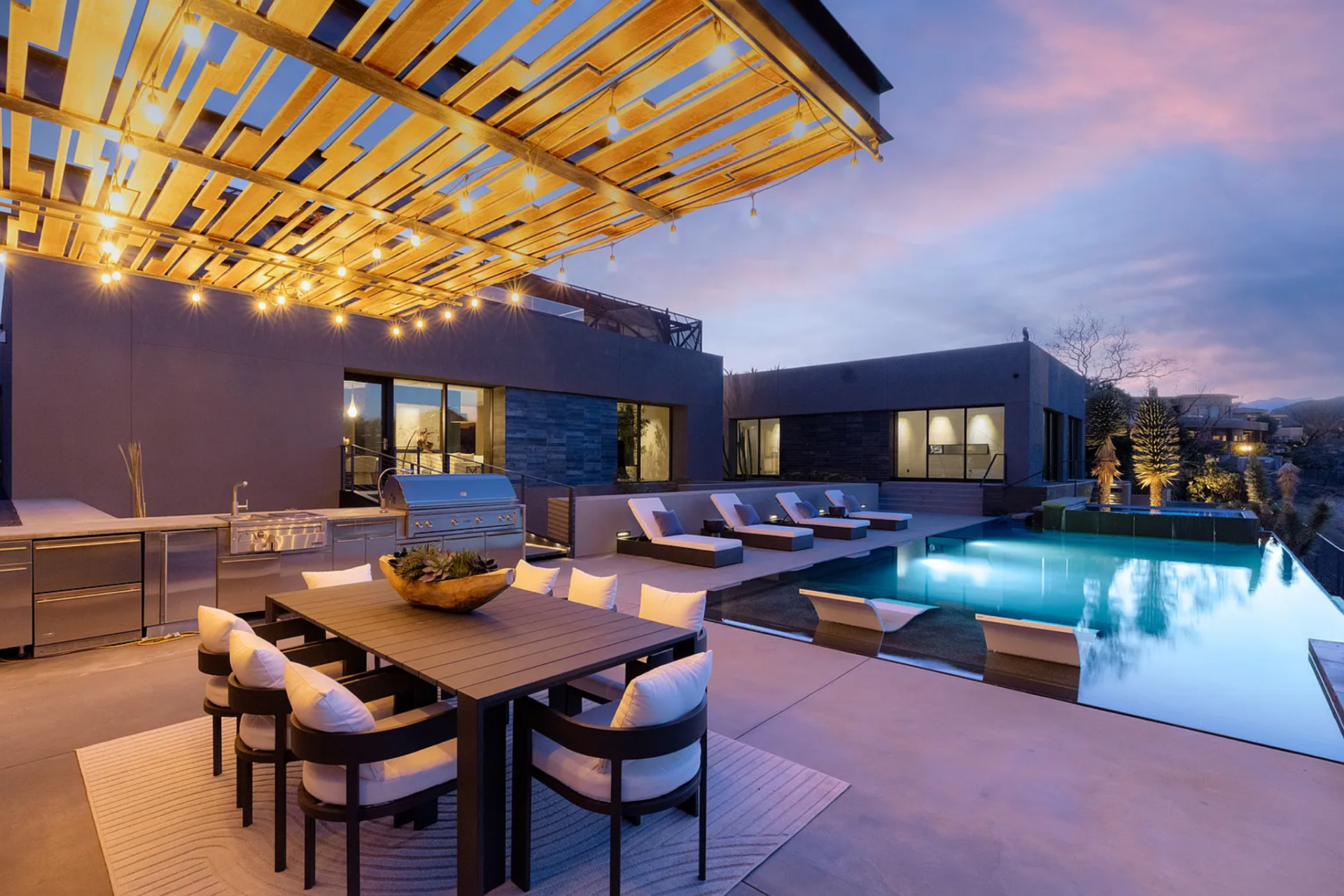 Next to the pool, a covered outdoor dining area sits beneath a slatted wood pergola, where integrated lighting adds a warm glow as the sun goes down. 