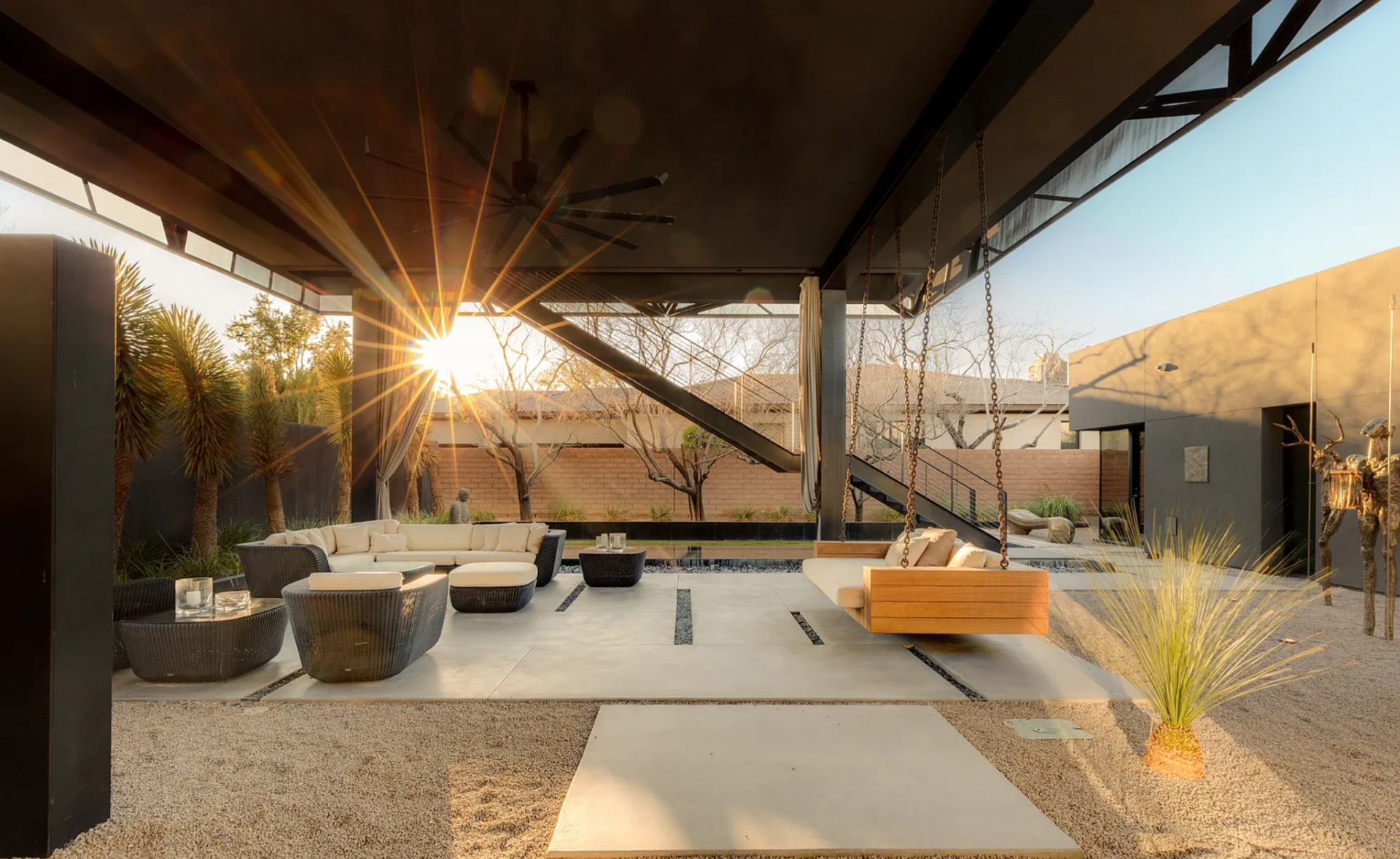 A covered lounge takes up most of the space with built-in seating and a suspended daybed, while clean concrete pathways cut through gravel landscaping.