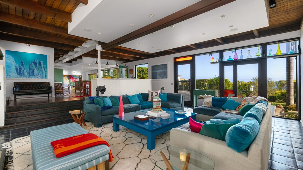 Walls of glass line two sides of the space, pulling in natural light and framing views of the surrounding greenery, while doors lead directly out to the backyard.