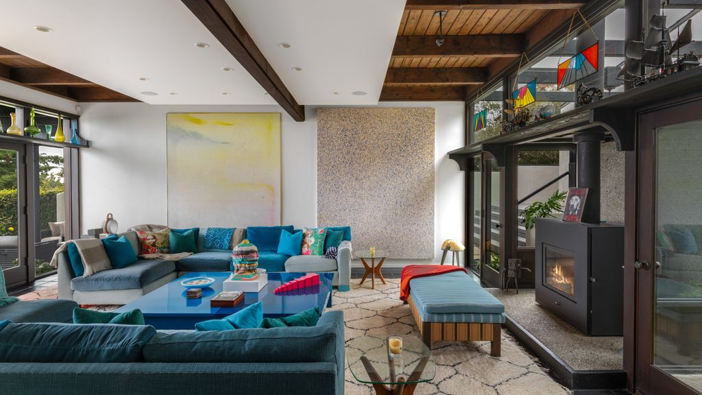 The room itself is organized around two colorful sectionals and a central coffee table, creating a grounded gathering space beneath exposed wood beams.