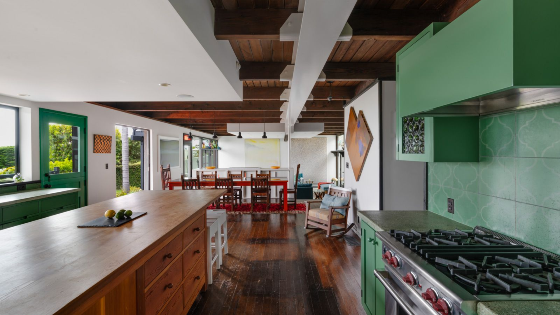 Green cabinetry wraps the perimeter and continues into floating upper cabinets, adding color while keeping sightlines open across the room.