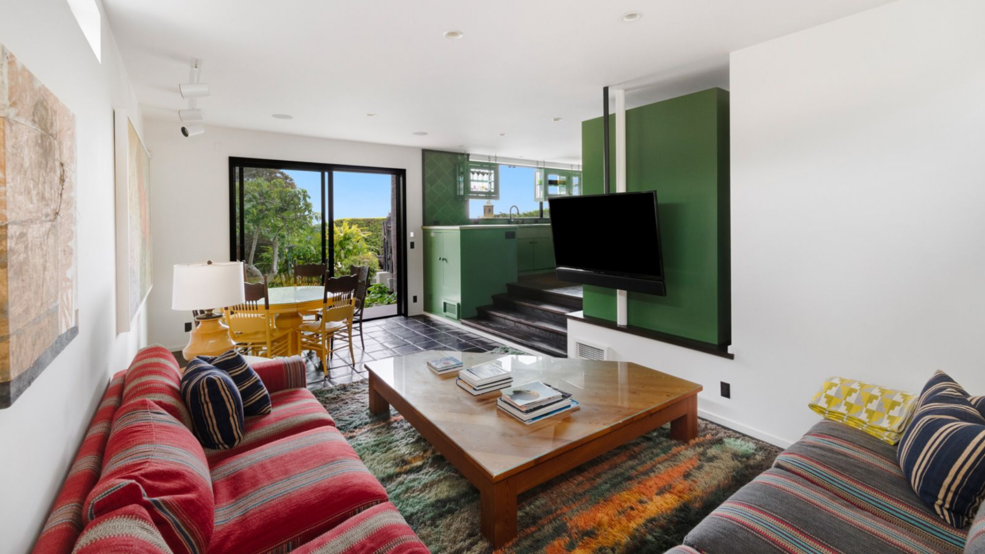 A wall-mounted sits across from stripped couches and a large coffee table, which have views that extend out to both the mountains and the ocean.