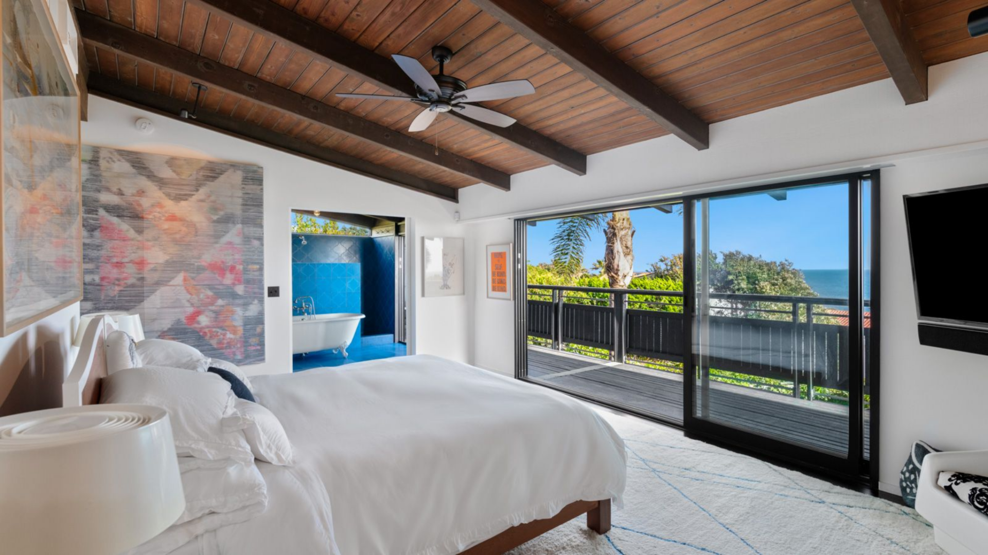 The second suite centers around a low-profile bed set against a clean white wall, with a large-scale artwork adding color above the headboard.