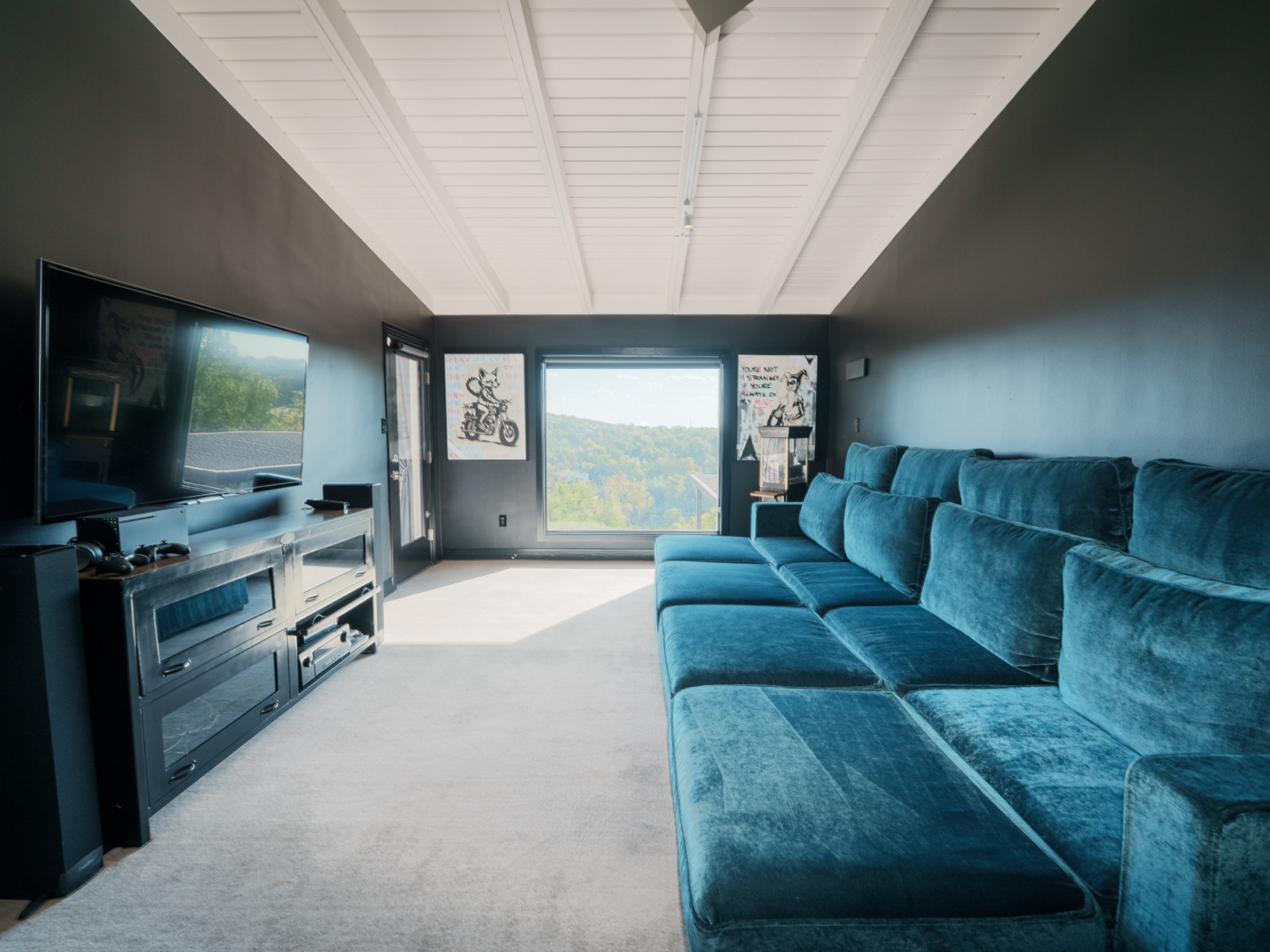 The media room has a darker, more intimate tone, with deep charcoal walls and a large sectional in rich teal velvet stretching nearly the length of the room. 
