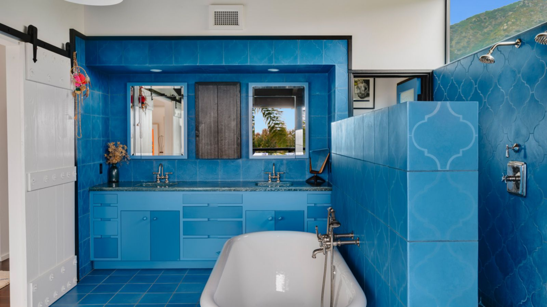 Along one side, a long vanity with dual sinks and matching blue cabinetry runs beneath two mirrors, with a stone countertop tying the elements together.
