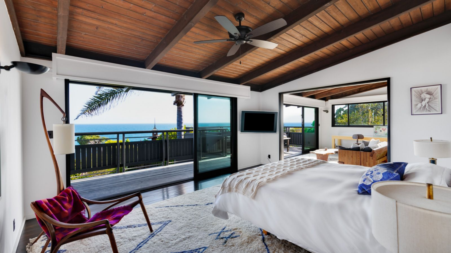 The first primary suite expands beyond a standard bedroom layout, beginning with a larger sleeping area framed by exposed beam ceilings.