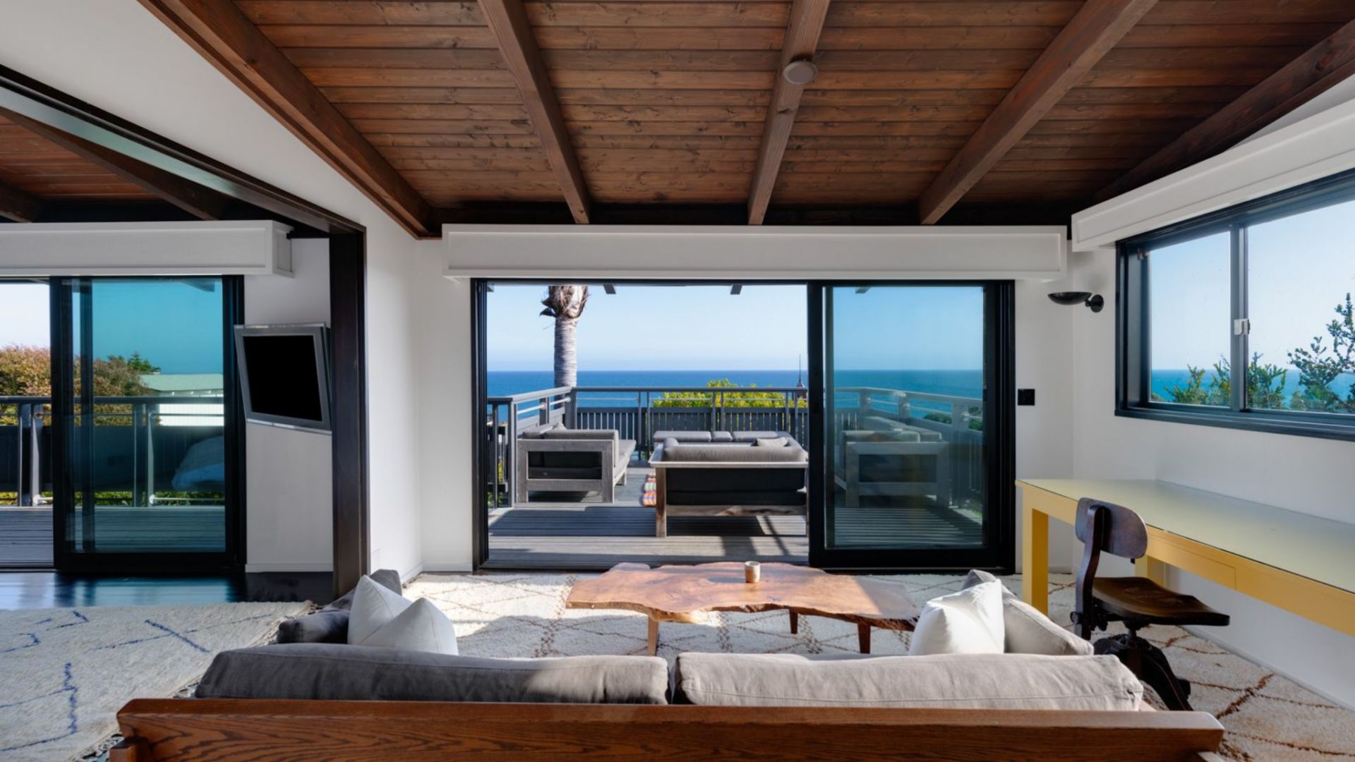 A sofa and coffee table are positioned to face the outdoor deck, with large sliding doors opening to a furnished terrace.