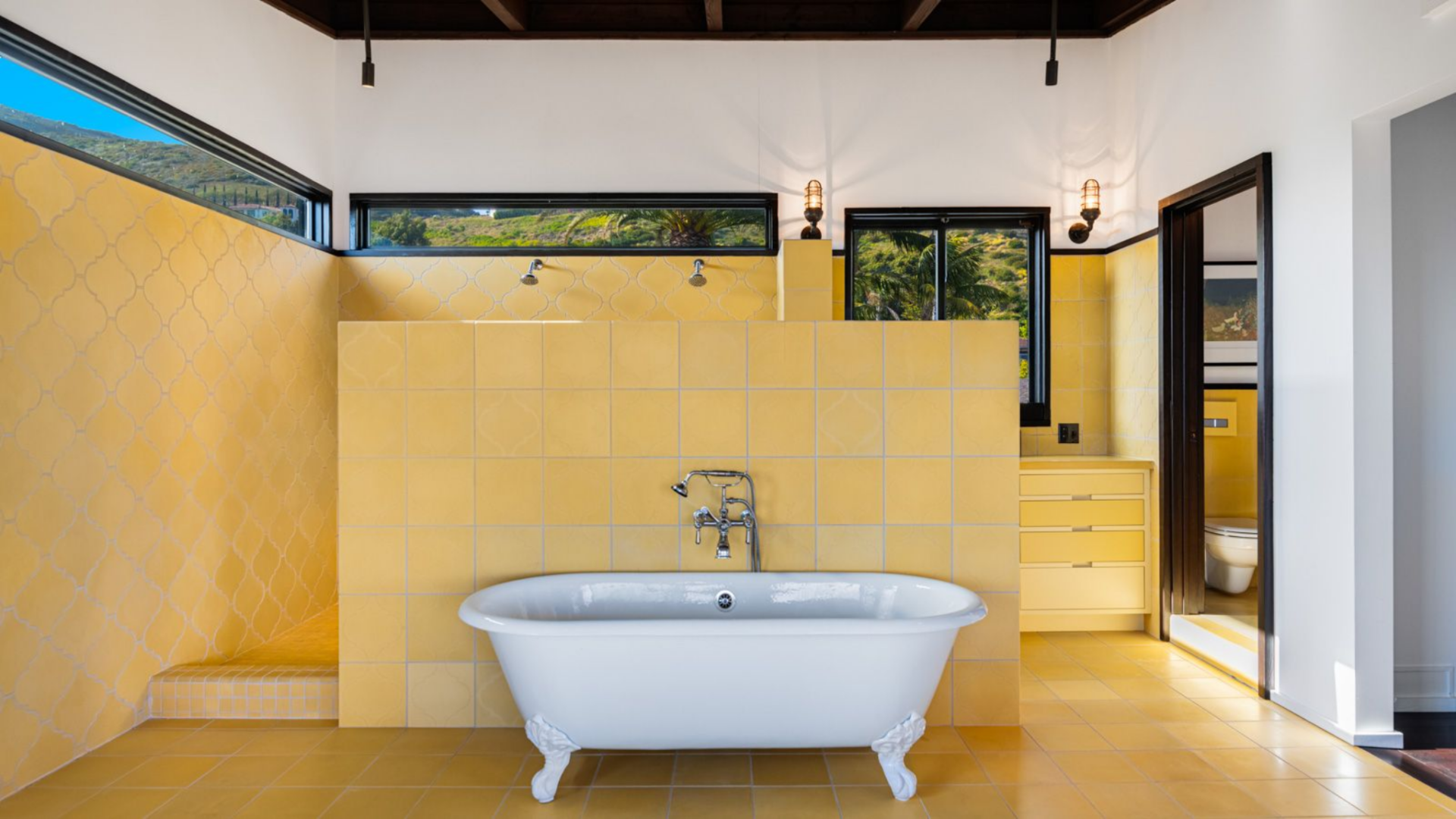 A freestanding tub is set against a tiled divider wall, with open shower areas on either side, creating a more segmented layout within a single open space.