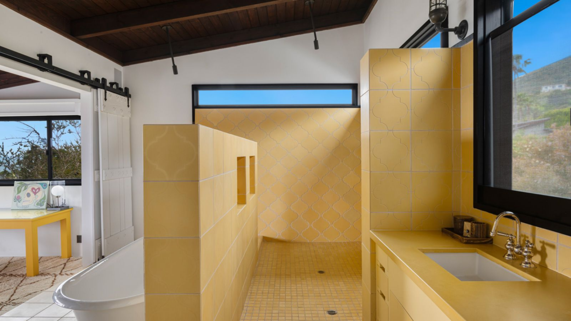 A matching yellow vanity with an integrated sink sits along one wall beneath a window, bringing in natural light from the other side of the house.