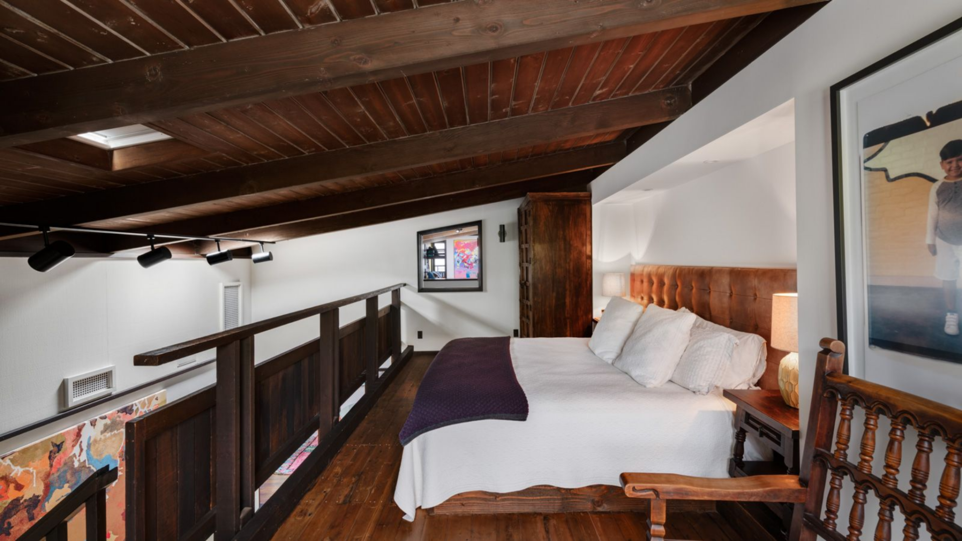Above the bar lounge, the lofted bedroom overlooks the entertainment space below, defined by a wood railing that runs along the edge of the mezzanine.