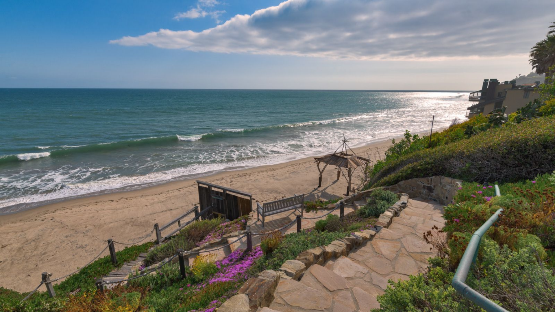 A stone-lined pathway leads from the yard down the bluff, transitioning into a private stairway that connects directly to the sand below.