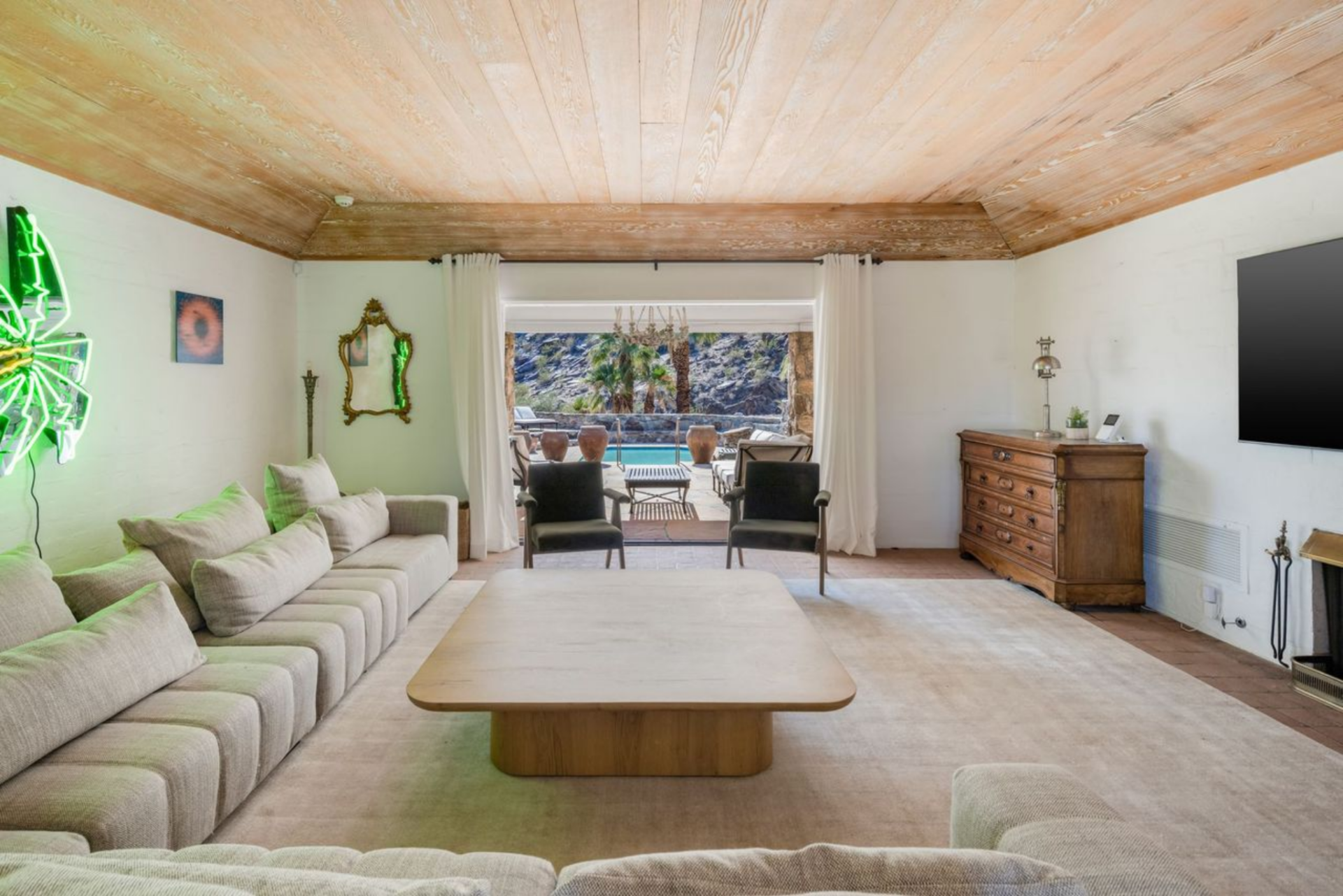 At the far end, full-width sliding glass doors frame a direct view out to the pool terrace, pulling the eye straight through the space and reinforcing the connection between the interior living area and the outdoors.
