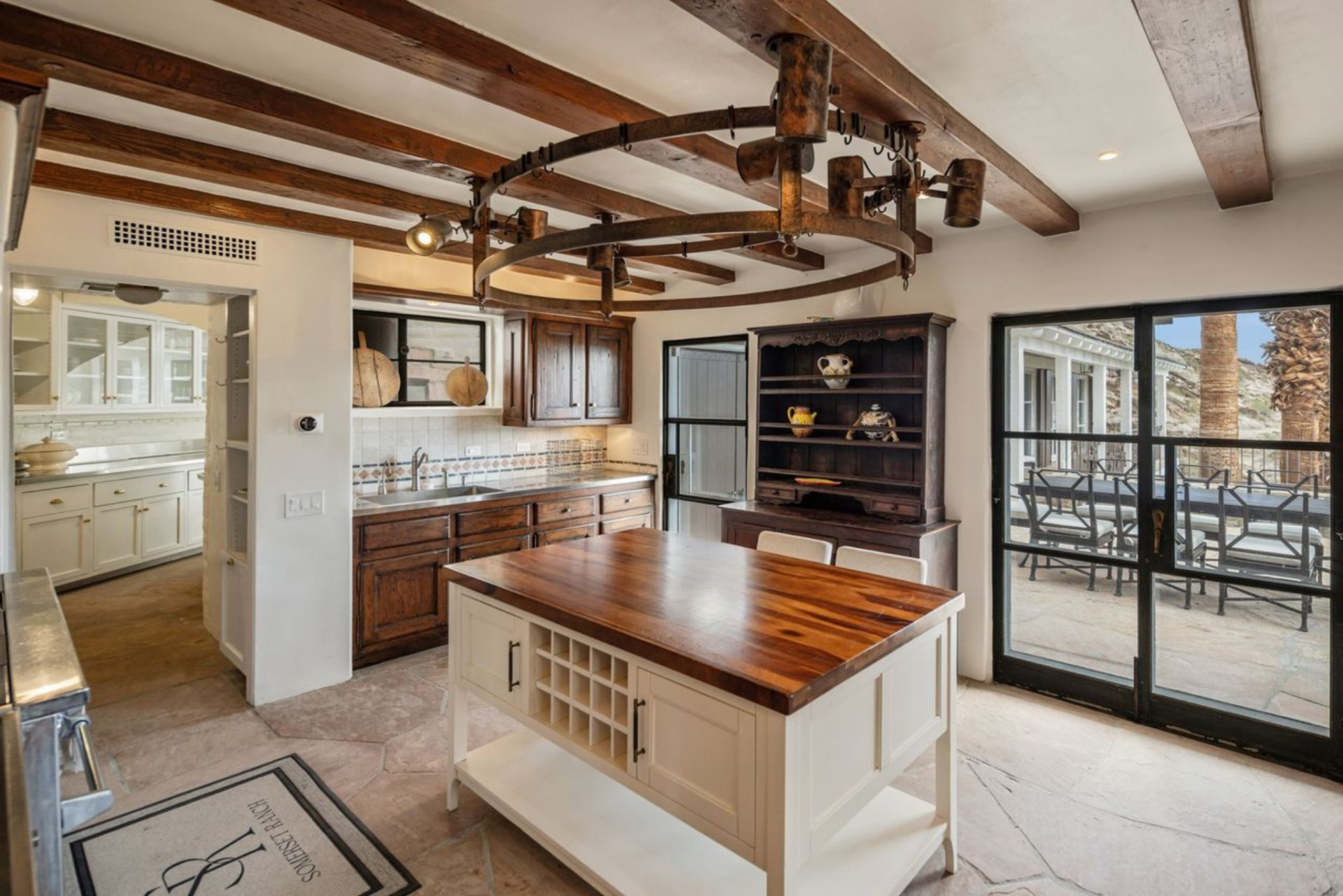 In the next room, the kitchen is laid out as a dual working space, with a primary cooking area anchored by a large professional-grade range and a secondary prep kitchen tucked around the corner.