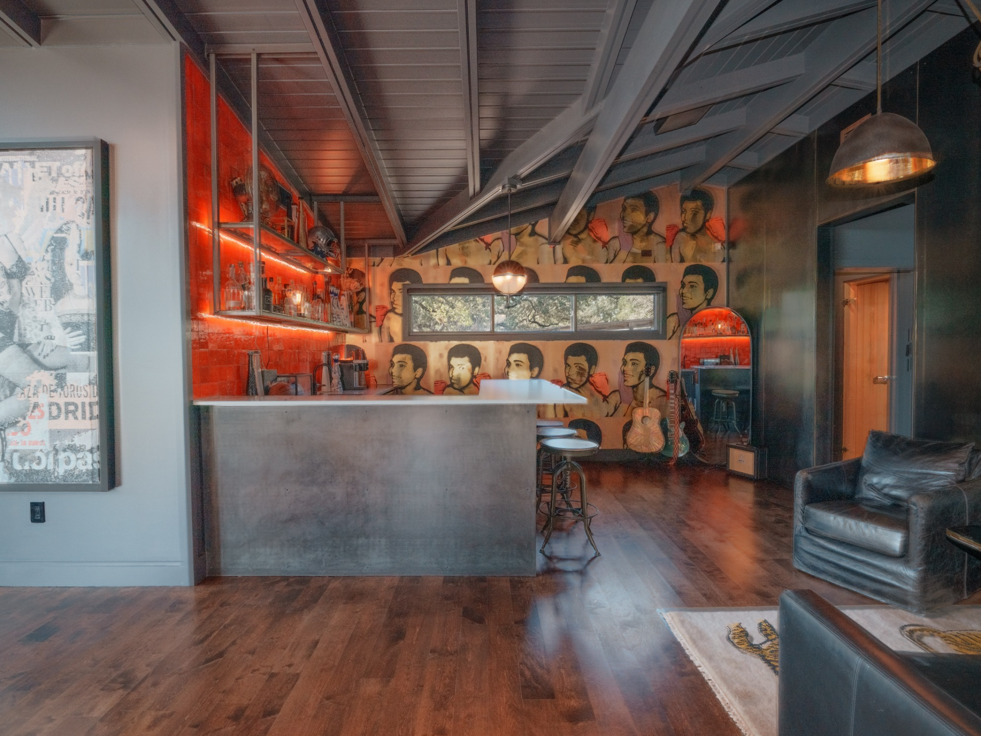The bar is wrapped in dark tones with a striking mural backdrop, and the space is illuminated by red under-cabinet lighting that highlights open shelving stocked with bottles and glassware.