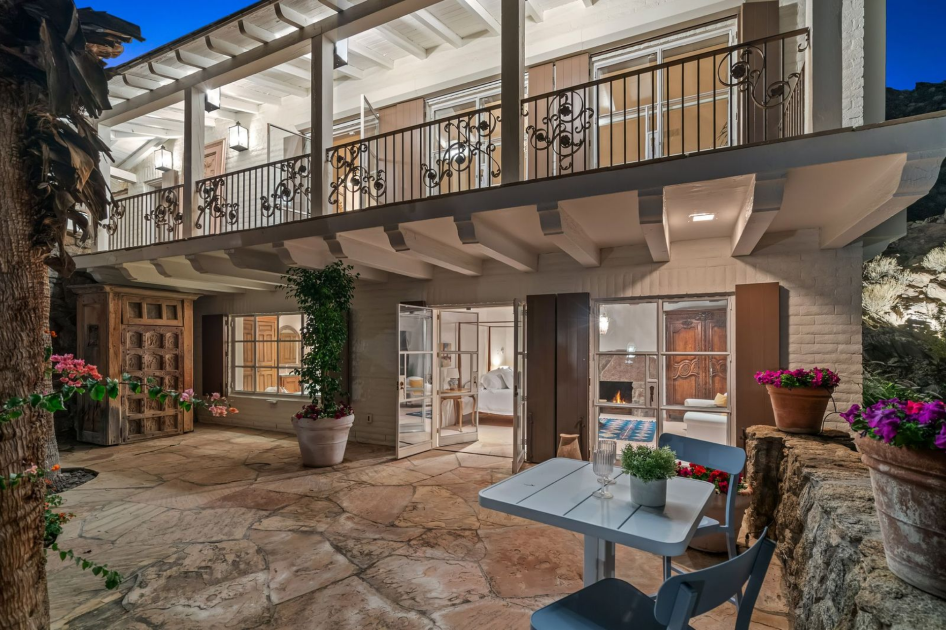Set within the hillside and arranged around a private stone courtyard, this guest villa has a covered upper balcony with decorative iron railings running the length of the structure, while below, a series of French doors opens directly into the courtyard, creating a layered indoor-outdoor layout.