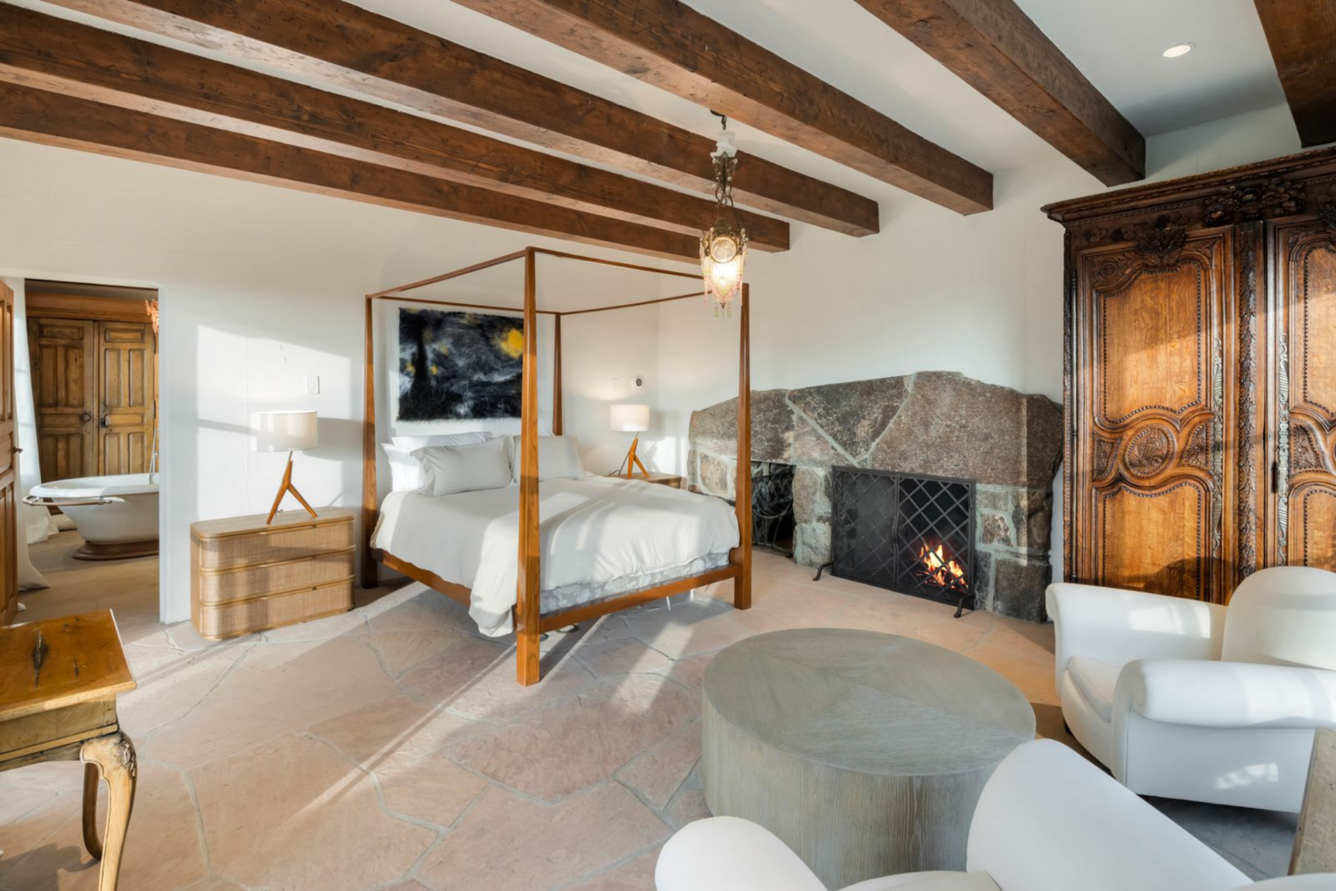 Inside, the bedroom features a four-poster bed positioned next to a substantial stone fireplace.